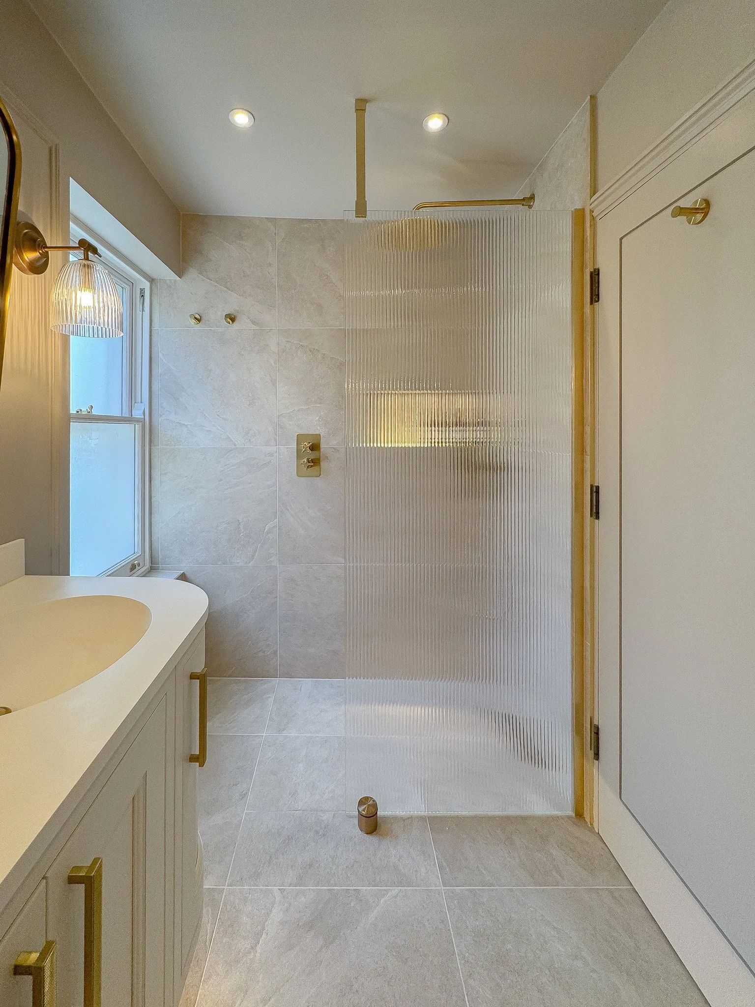 Luxury walk-in shower with fluted glass screen, brushed brass fittings, large-format stone tiles and integrated illuminated niche