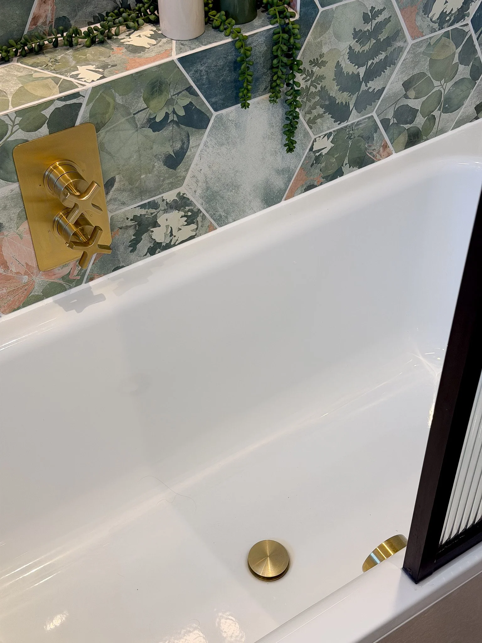 Detail of freestanding bath with brushed brass bath controls and botanical patterned wall tiles in a bespoke luxury bathroom