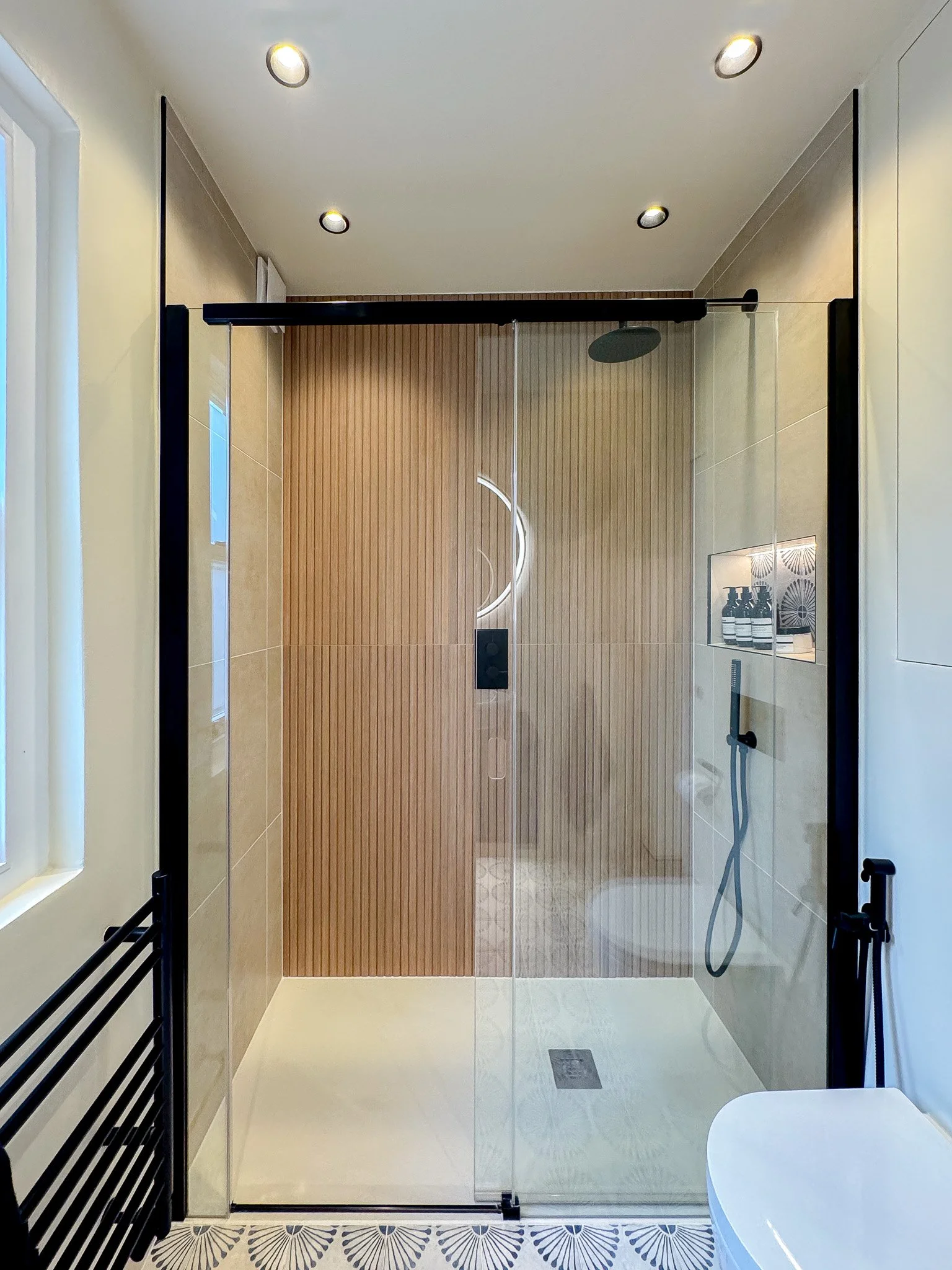 Walk-in shower with fluted wood-effect tiles, black fittings and glass enclosure in North London