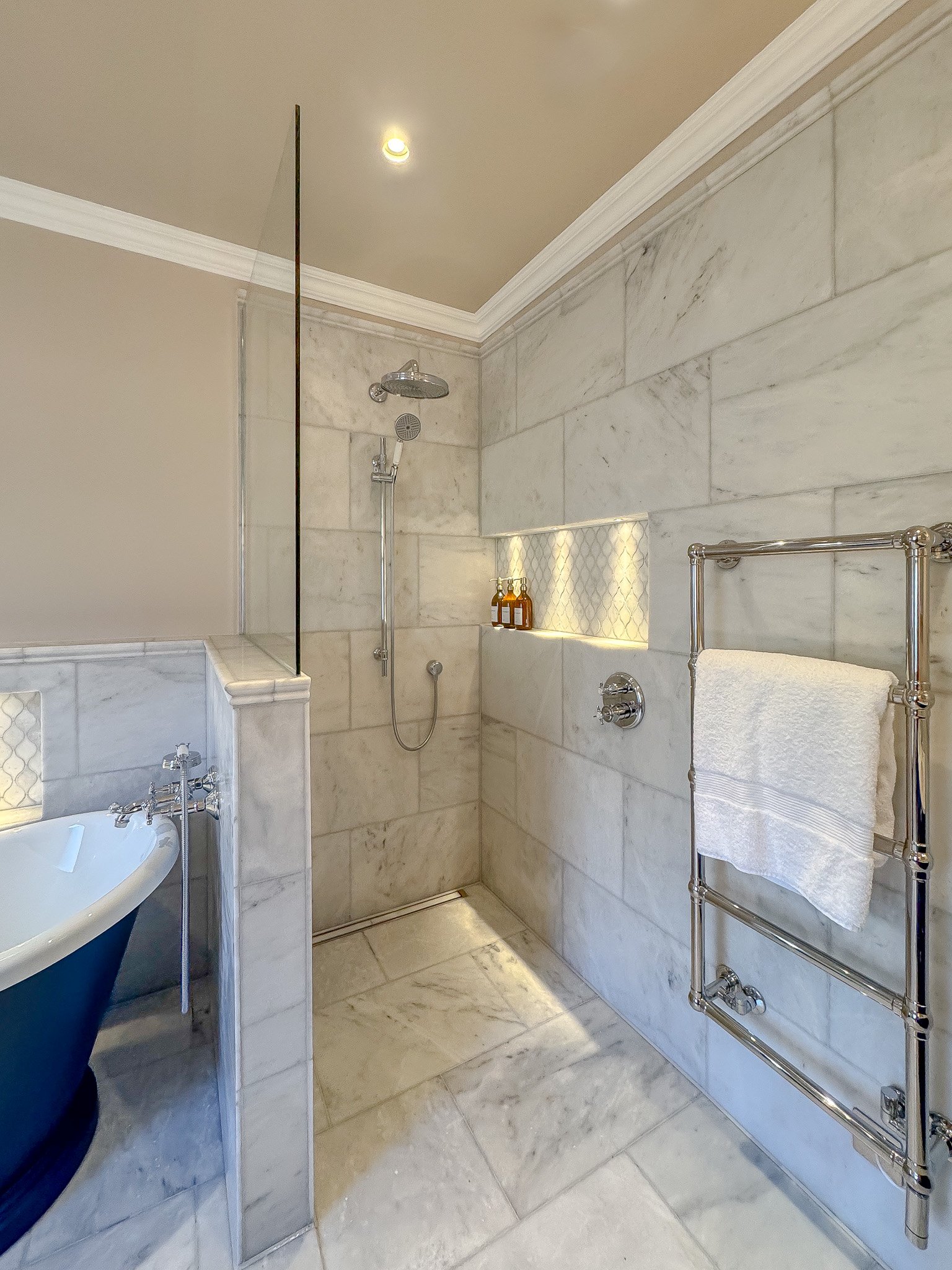 Luxury marble walk-in shower with chrome rainfall shower, recessed illuminated niche and glass screen in a classic bespoke bathroom design by North Arch Bathrooms, London