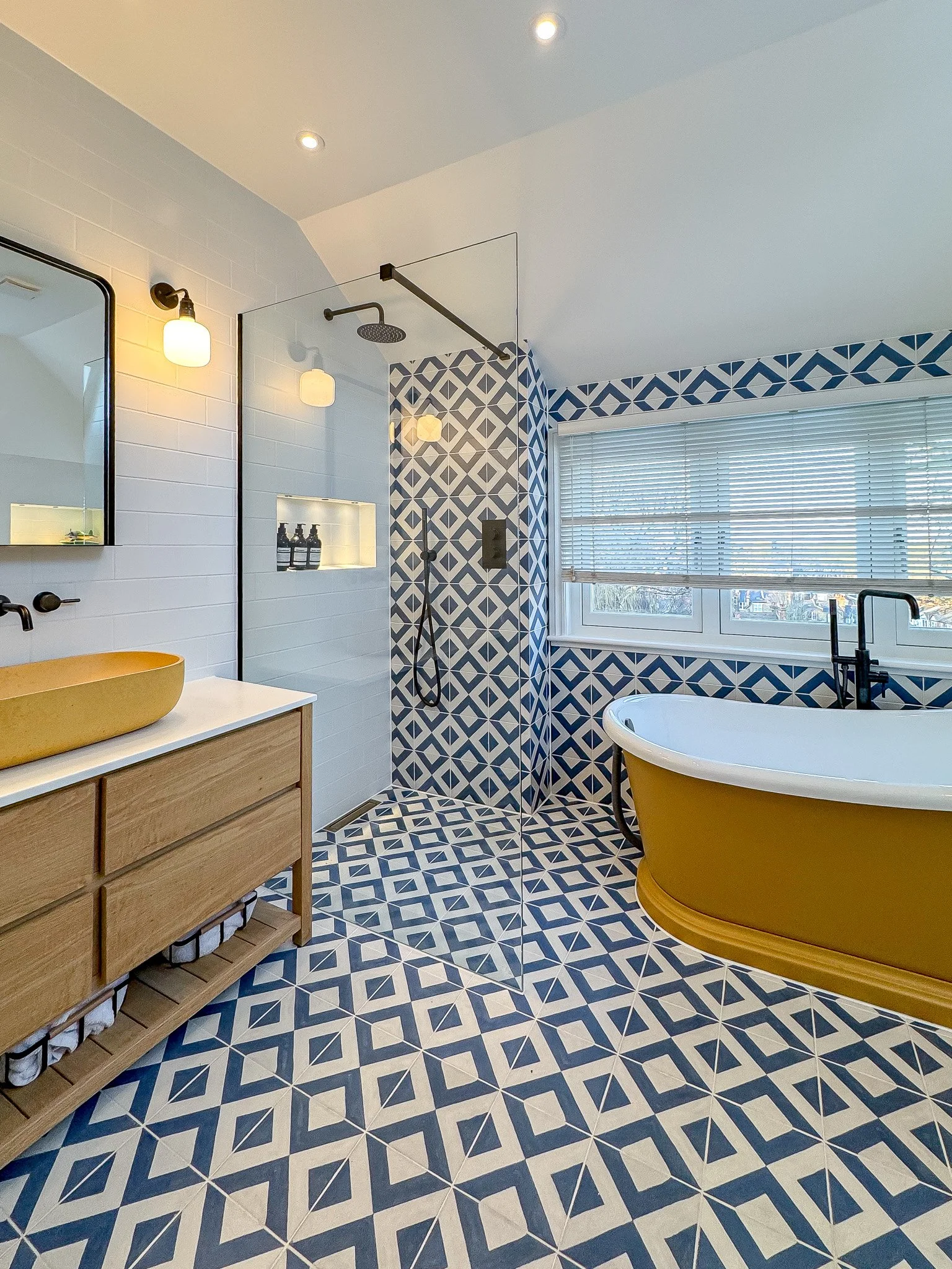 Colourful family bathroom with patterned blue floor tiles, walk-in shower, freestanding bath and timber vanity unit
