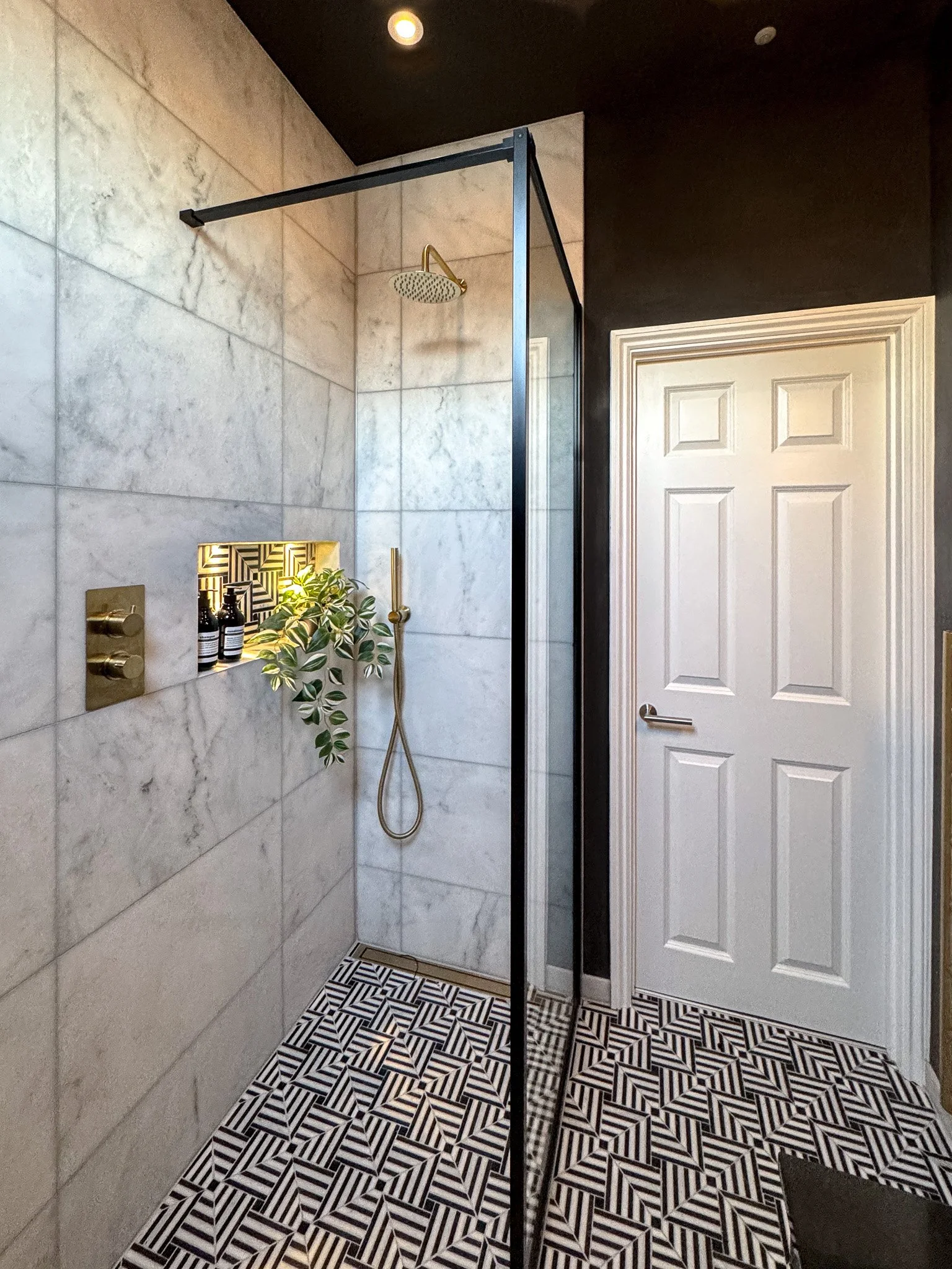 Statement walk-in shower with marble wall tiles, black framed glass screen, brass shower fittings and geometric patterned floor tiles