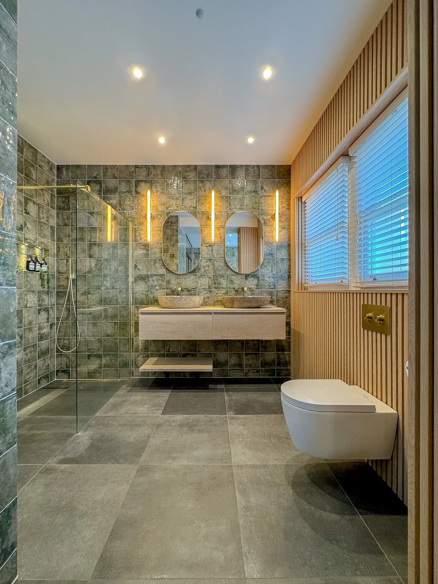 Contemporary bathroom with double stone basins, green textured wall tiles, walk-in glass shower and timber slatted feature wall