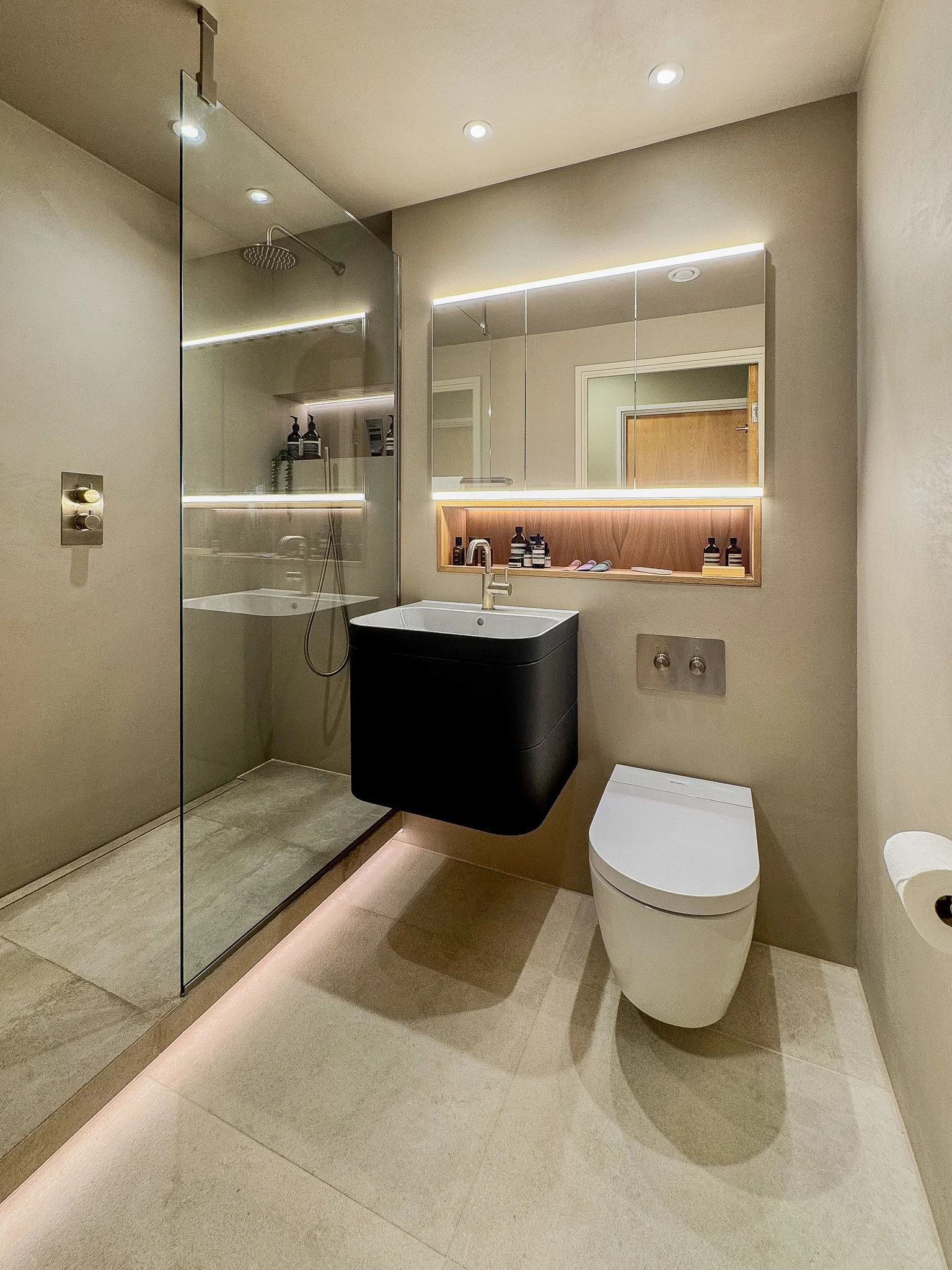 Modern luxury bathroom design with walk-in glass shower, wall-hung vanity unit and illuminated mirror by North Arch Bathrooms in North London