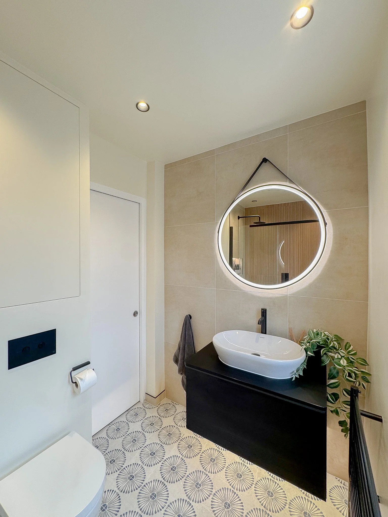 Modern bathroom vanity with matte black unit, countertop basin, circular illuminated mirror and patterned floor tiles in a contemporary bespoke bathroom.