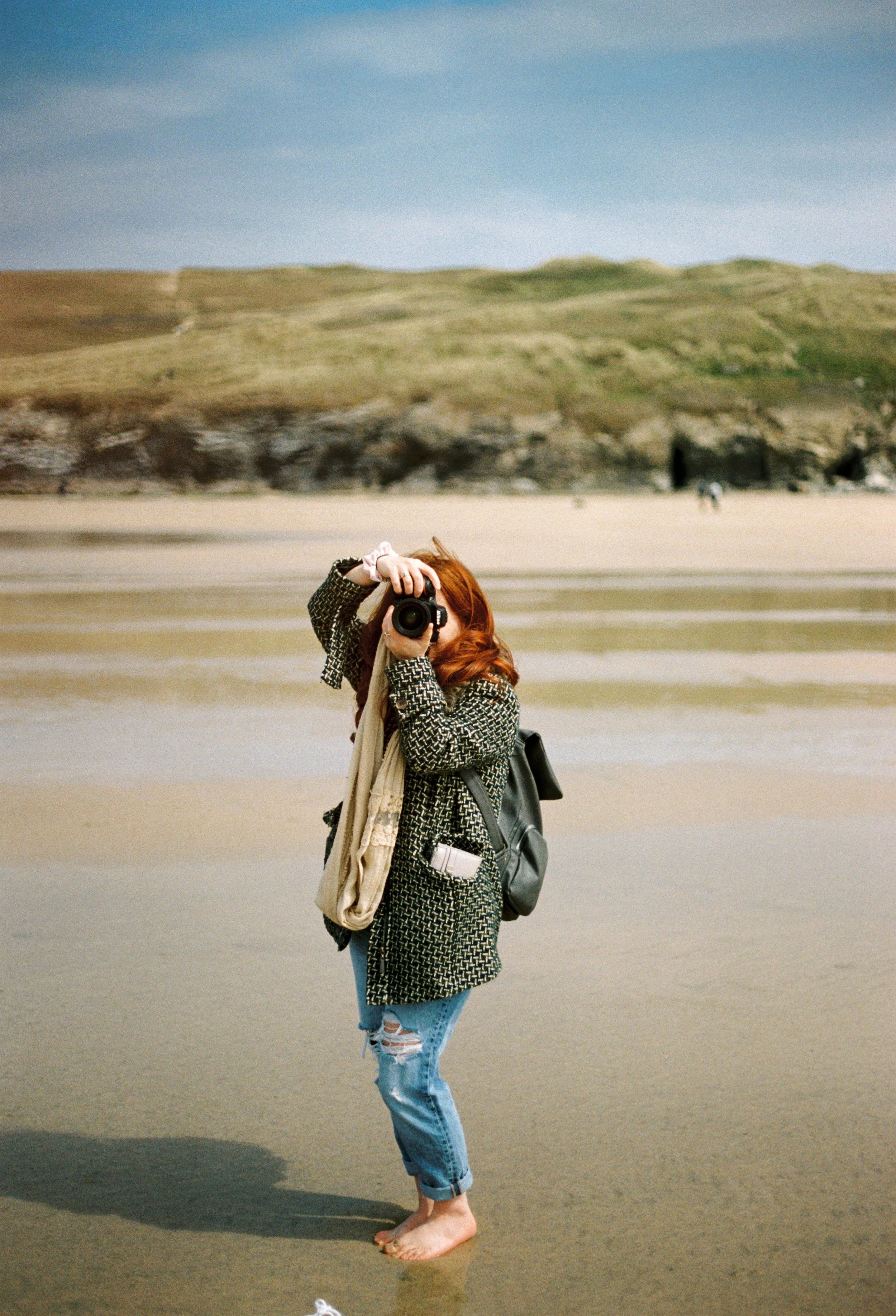 redhead photographer woman taking a photo using Nikon camera on beach in Cornwall, image taken on film camera
