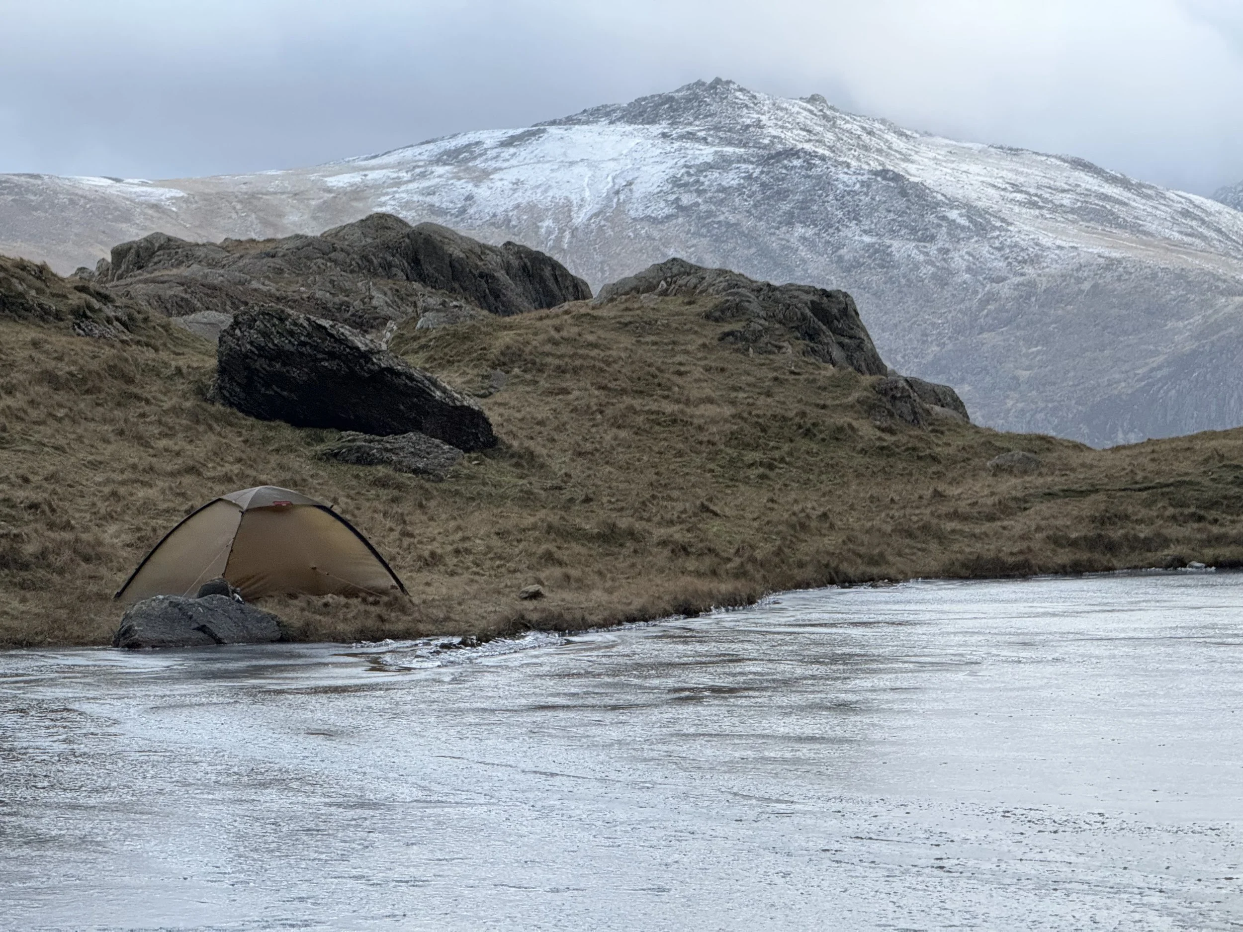 Tent by a frozen lake with snow-covered hills in the background.