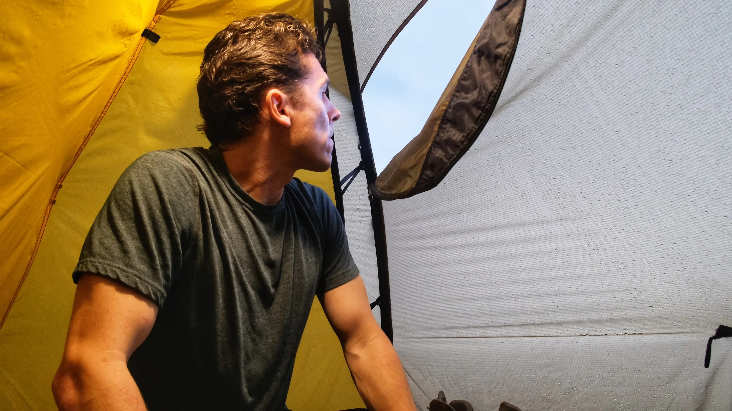 Man sitting inside a yellow tent looking out through a window.