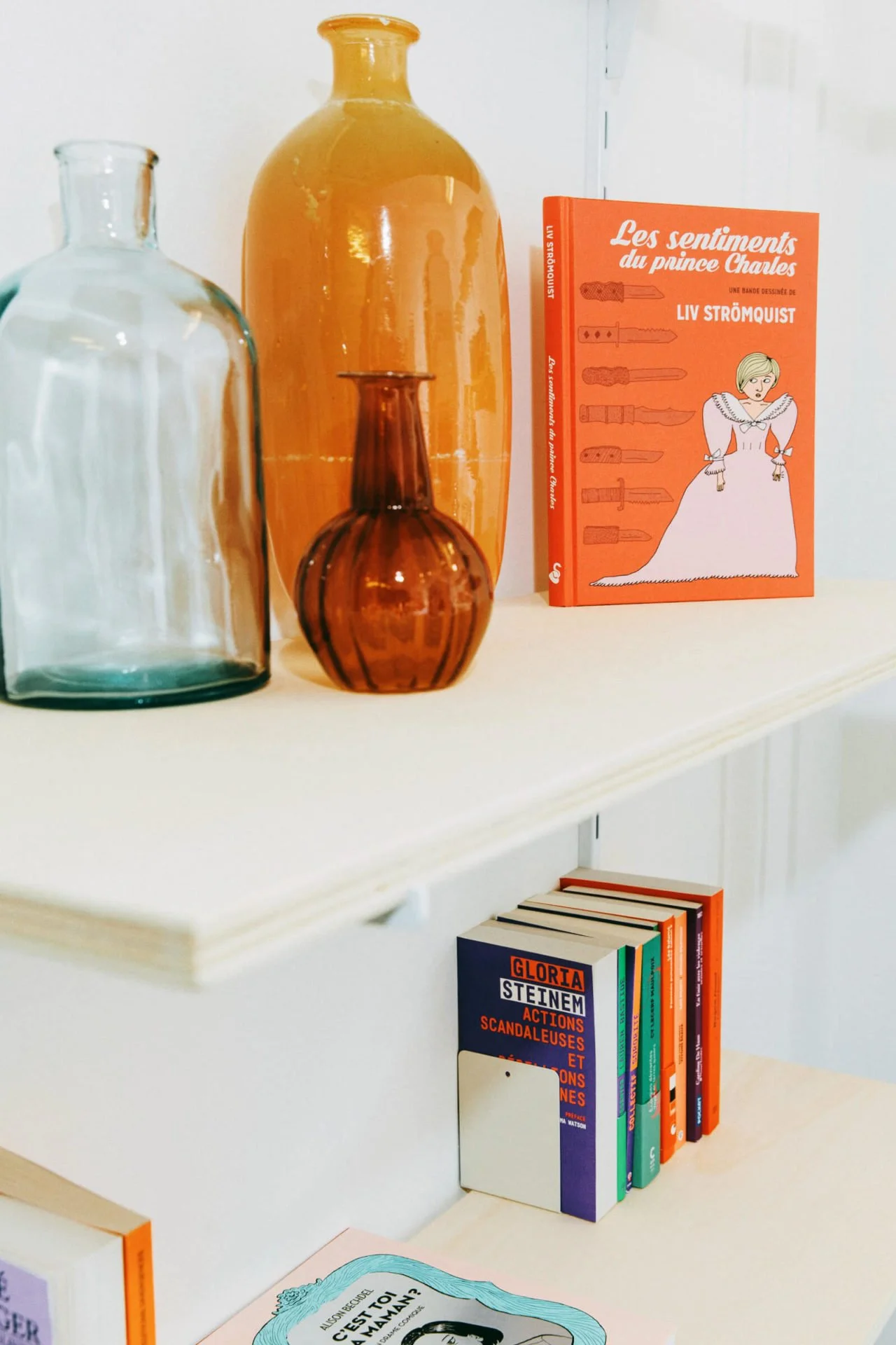 Livres colorés sur une étagère avec des bouteilles en verre de différentes tailles et couleurs.
