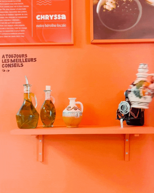 Une étagère avec trois bouteilles en verre, une carafe en céramique avec des motifs traditionnels, et une machine à café sur fonds orange avec affiches publicitaires