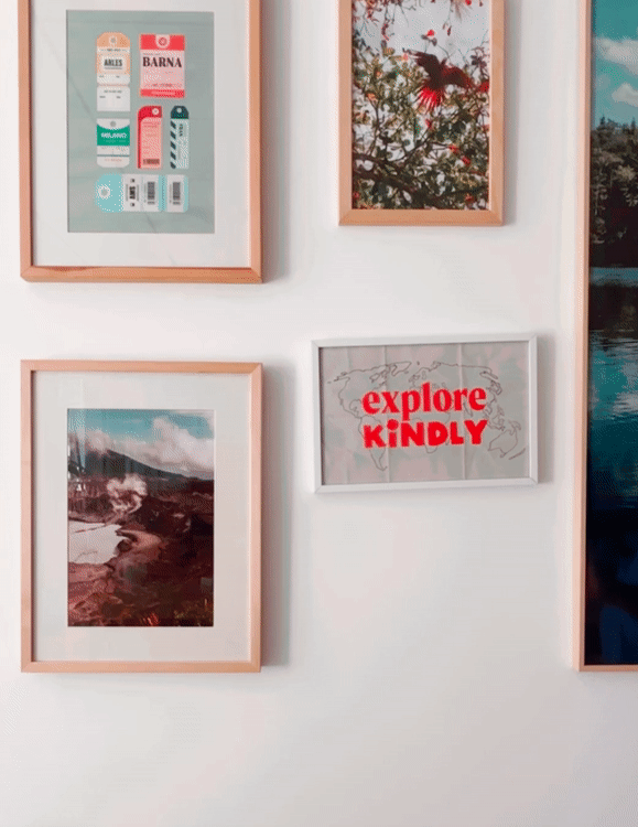 Une collection de cadres photos suspendus sur un mur blanc, comprenant des images de paysages, une affiche avec le texte "explore KINDLY" en rouge, et d'autres photos de nature et de voyage.