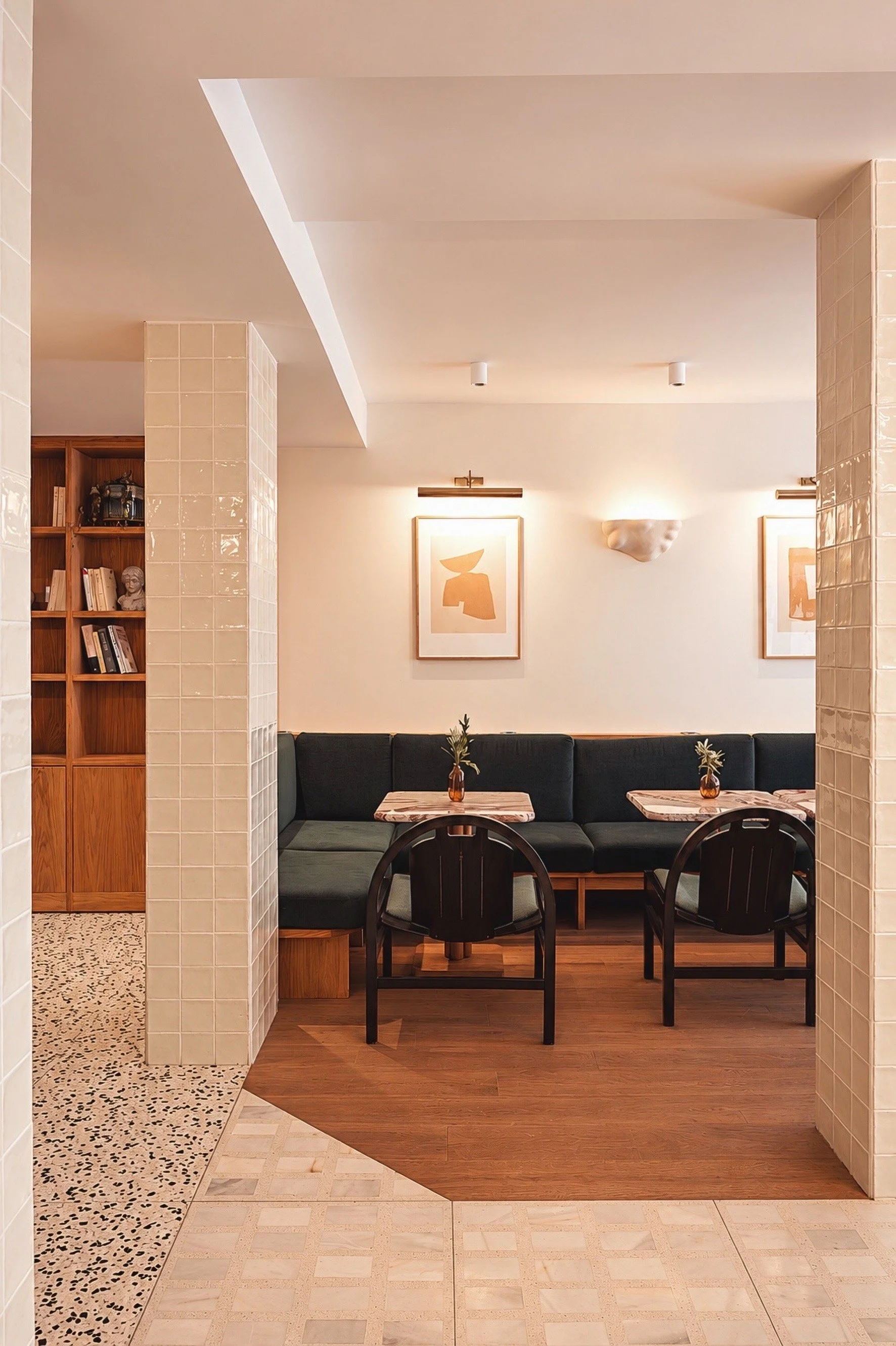 Un coin salon avec un canapé noir, deux tables basses en marbre avec des vases et des plantes, murs ornés de deux œuvres d'art abstraites, et un mur en pierre beige