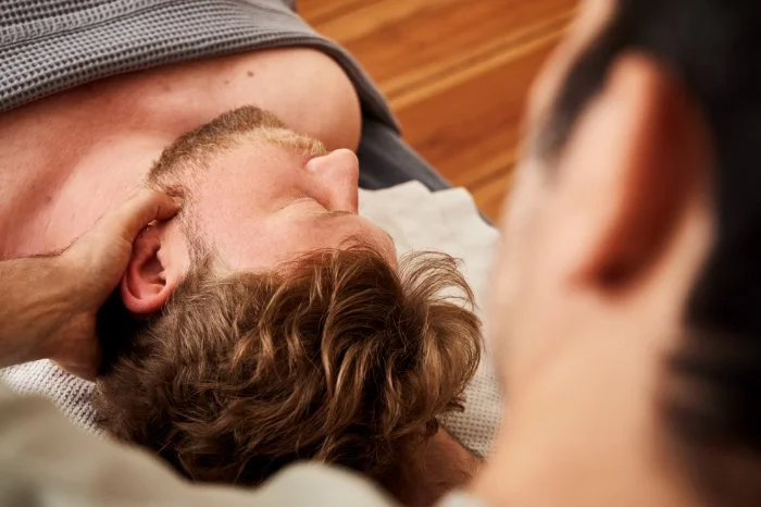 Ein Mann liegt entspannt auf dem Rücken auf einer Behandlungsliege. Sein Kiefer wird therapeutisch behandelt.
