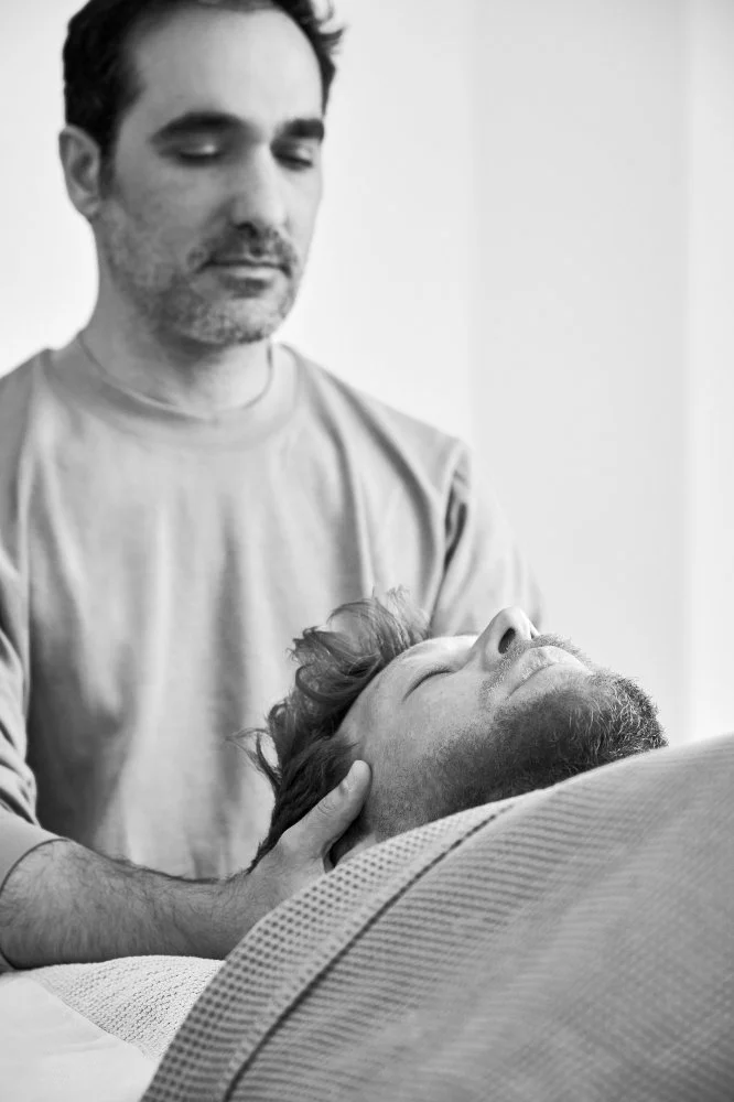 Zwei Männer, einer mit geschlossenen Augen, der andere liegt und wird am Kopf gehalten. Schwarz-Weiß-Foto.