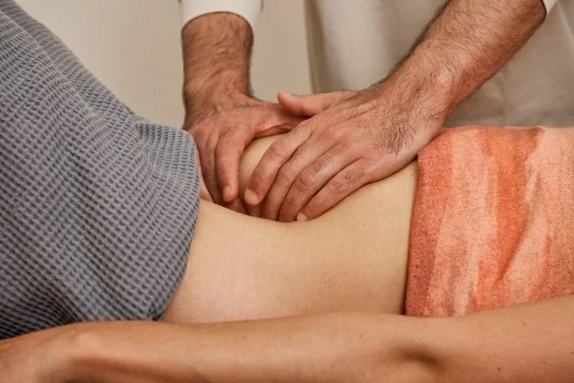 Zwei Hände massieren den Bauch einer Person, die auf dem Rücken liegt.