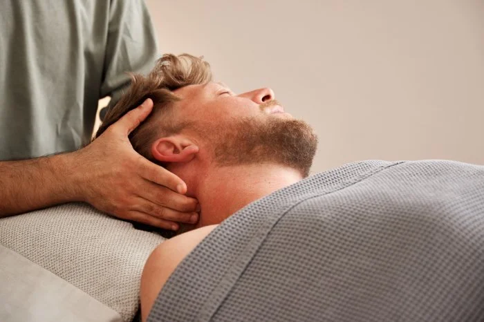 Mann erhält Nackenbehandlung, Nahaufnahme des Kopfes und der Hände des Osteopathen.