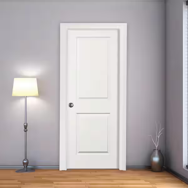 A white interior door in a gray wall with a silver doorknob, next to a floor lamp with a white shade and a metallic vase with a white branch inside.