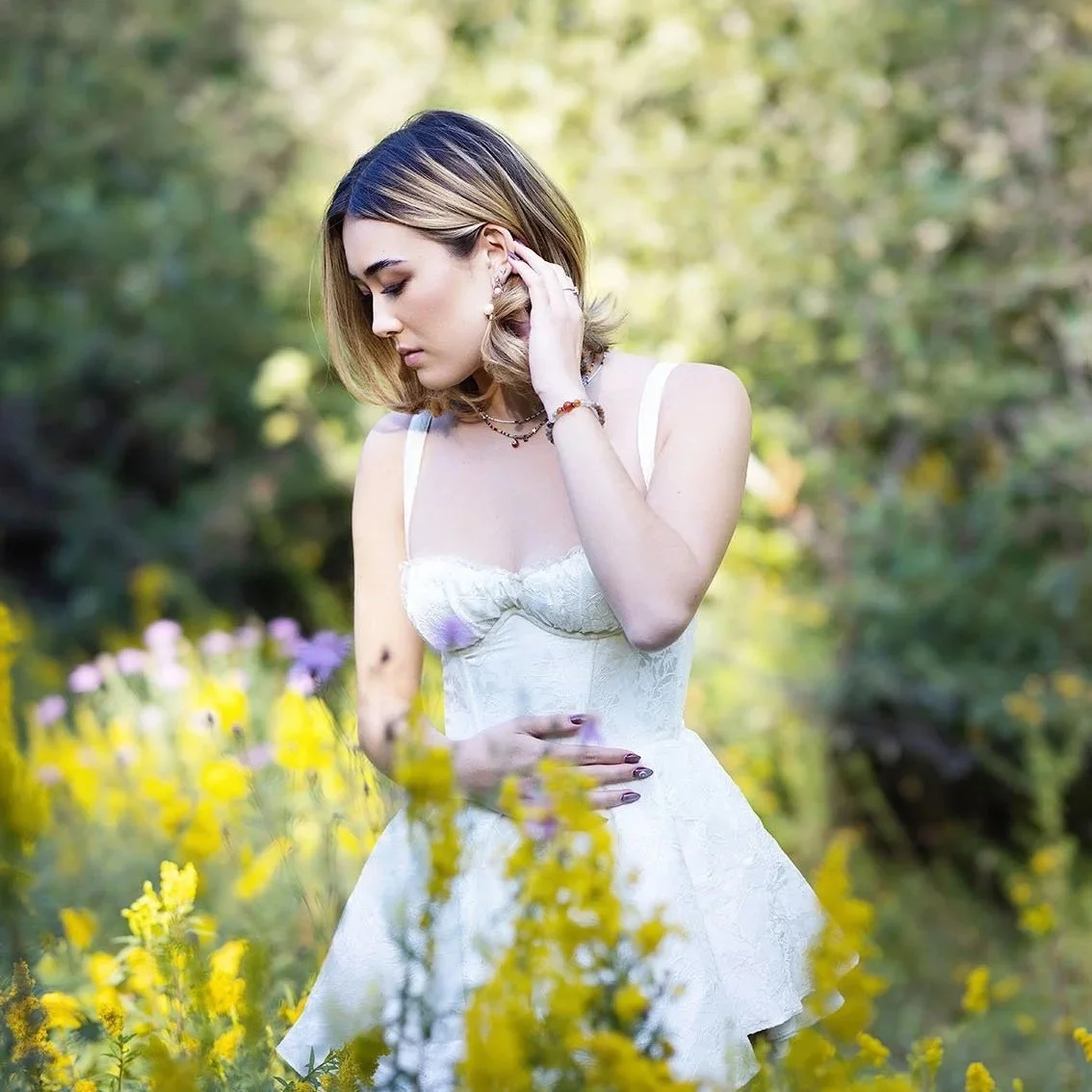 Senior portrait photographer, Beauclair Photography, serving Seattle shares image of senior portrait of girl in white dress among wild flowers in white dress, looking down