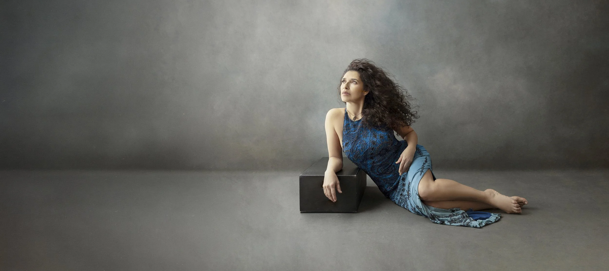 timeless custom portraits of women, families, maternity and children.  Woman lying down looking towards the light wearing blue dress in a fine art portrait.
