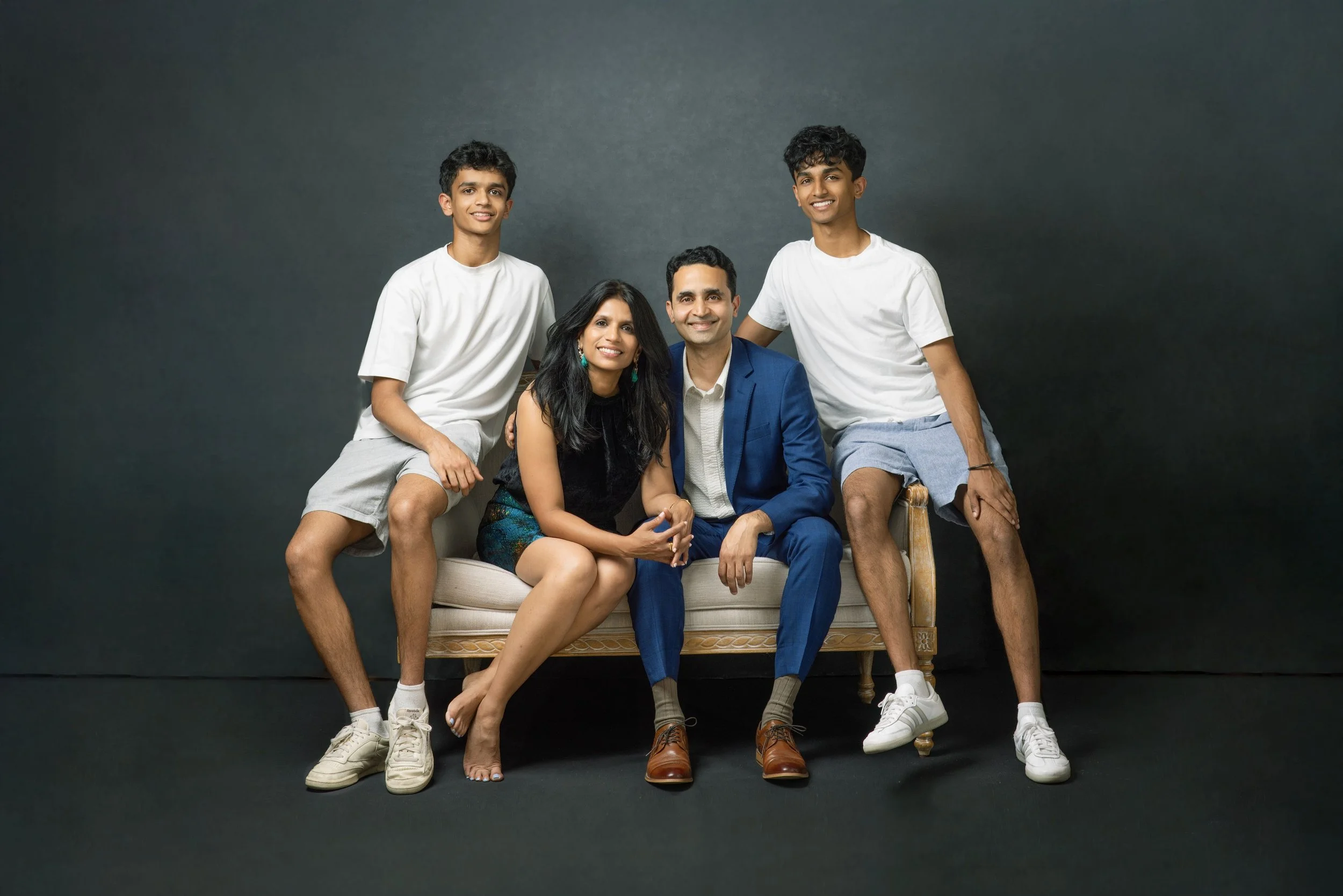 Family portrait in studio of two older teen boys and their parents on small couch