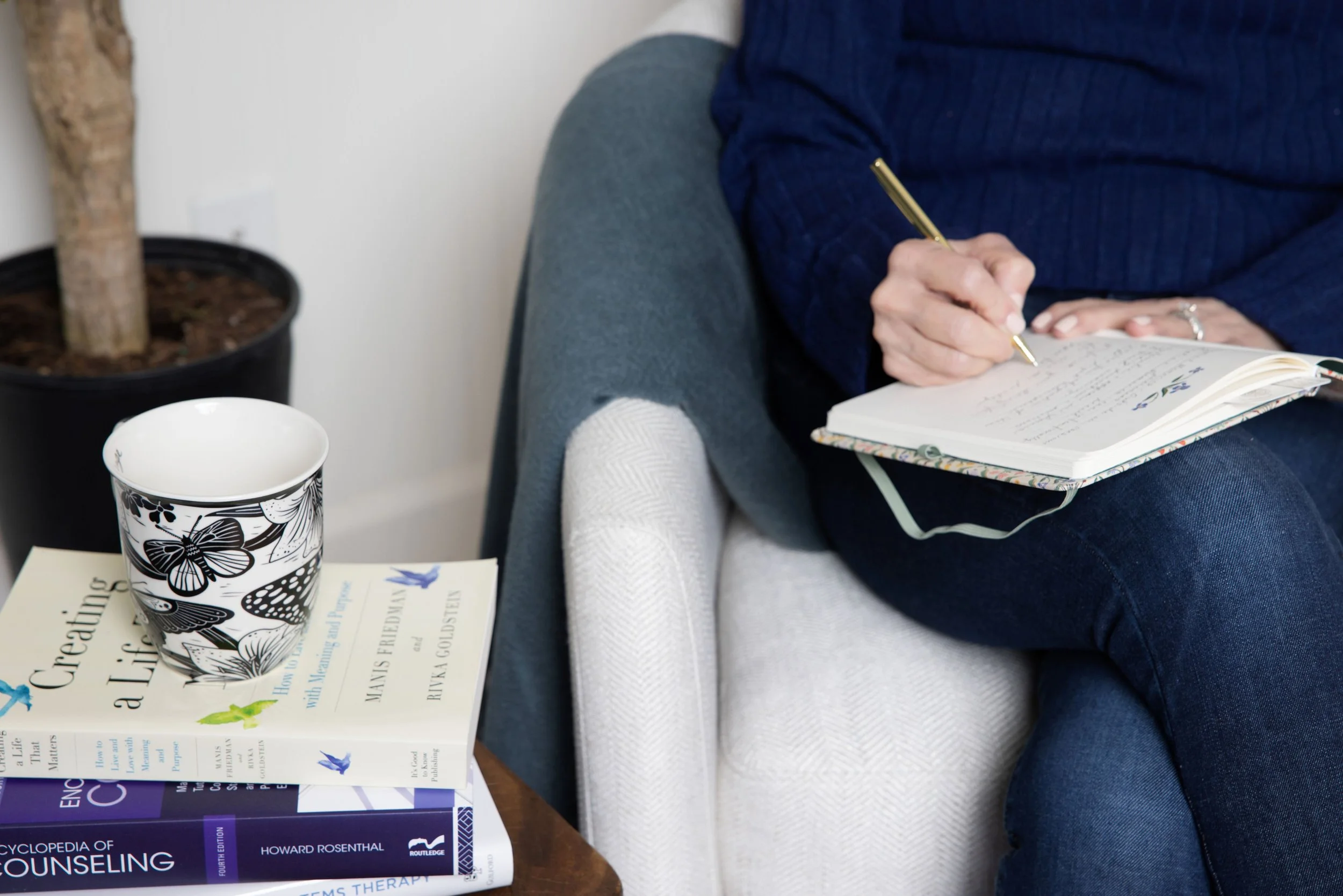 female author writes in a journal with a teacup and stack of books along side