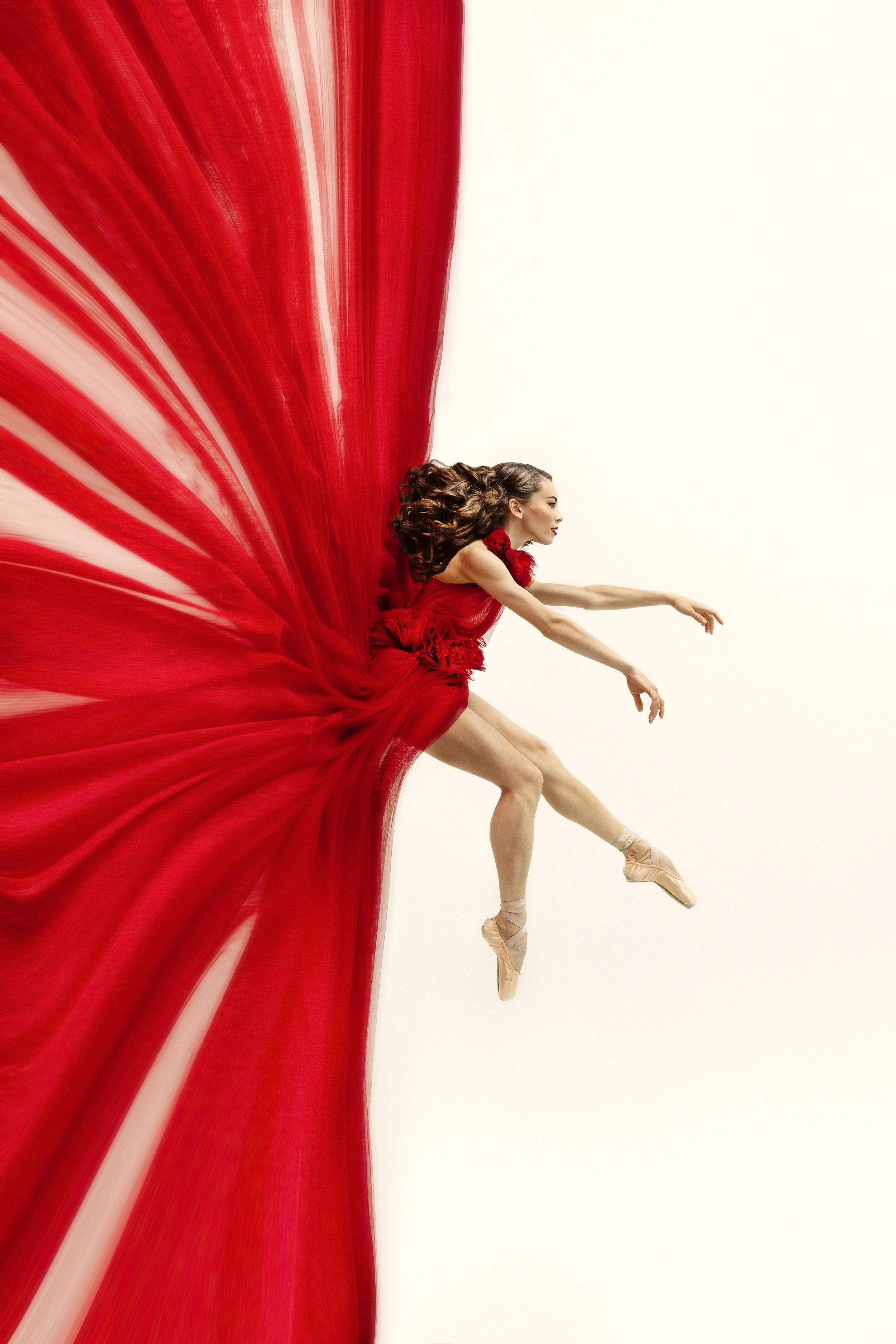 Dancer in red dress hanging from wall suspended with arms out