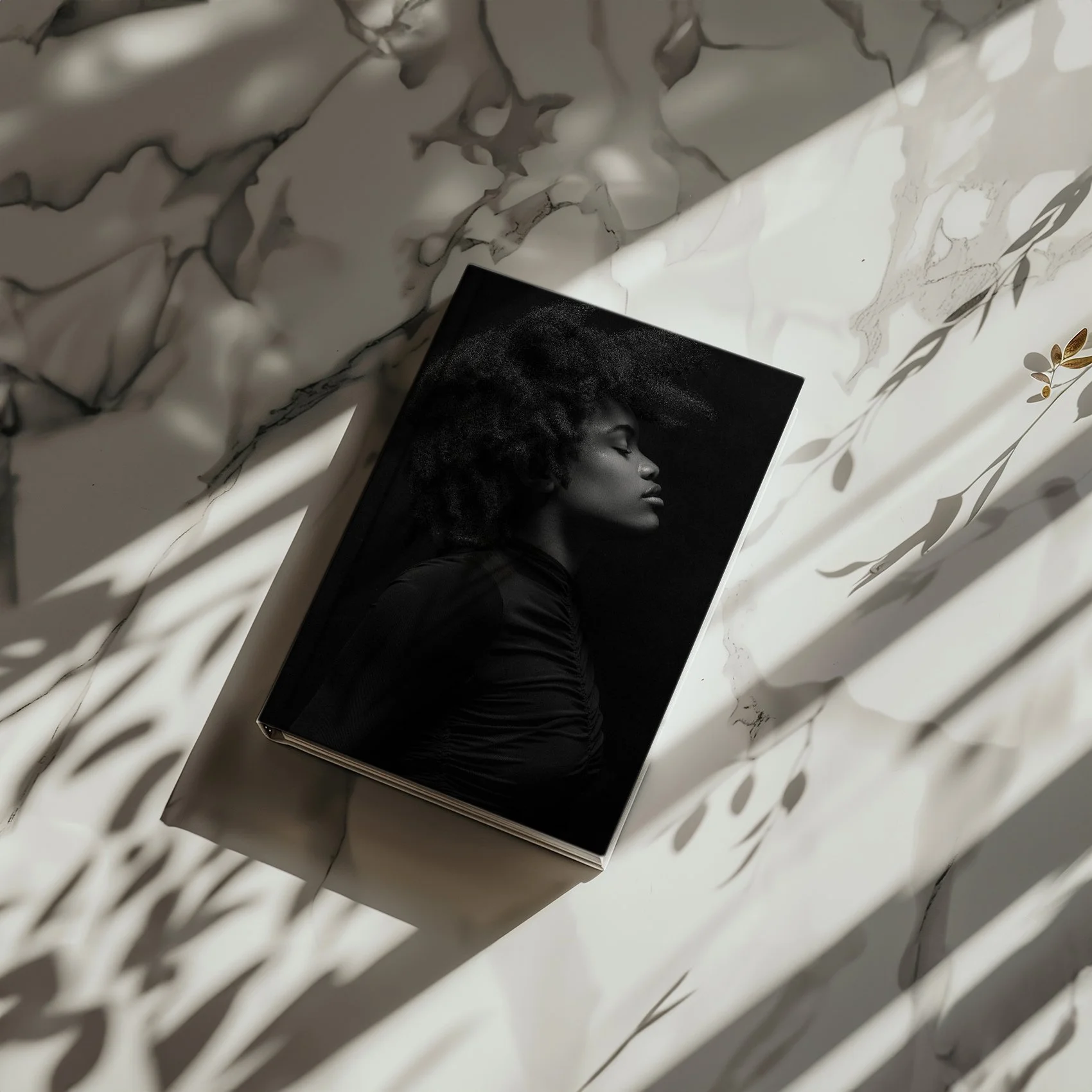 A black and white photograph of a woman with curly hair, profile view, on a book cover, resting on a white marble surface with shadows of leaves cast across it.