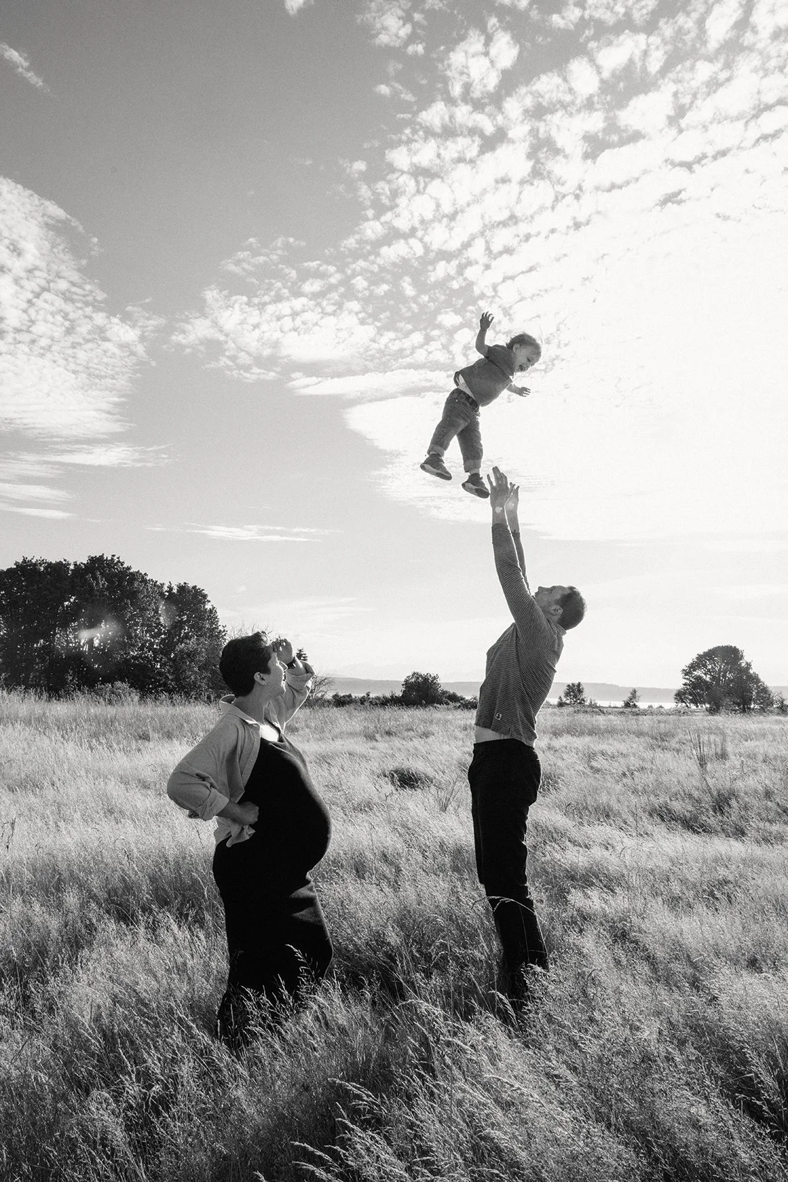 A family of three outdoors in a grassy field at Discovery park for maternity portraits near me