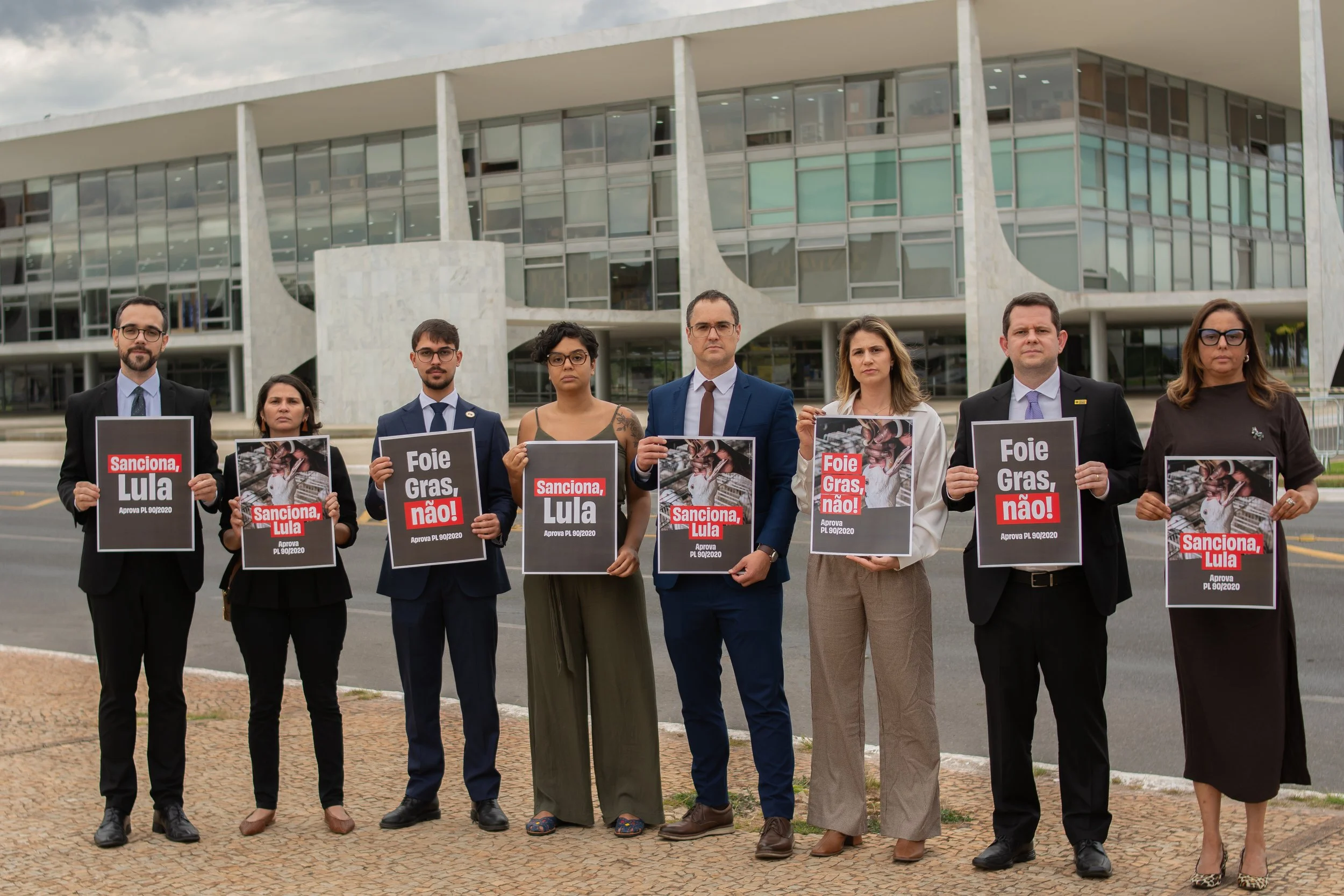 A group of animal welfare advocates standing in front of the Brazilian National Congress holding signs that read "Sanciona, Lula" and "Foie Gras, Não!"