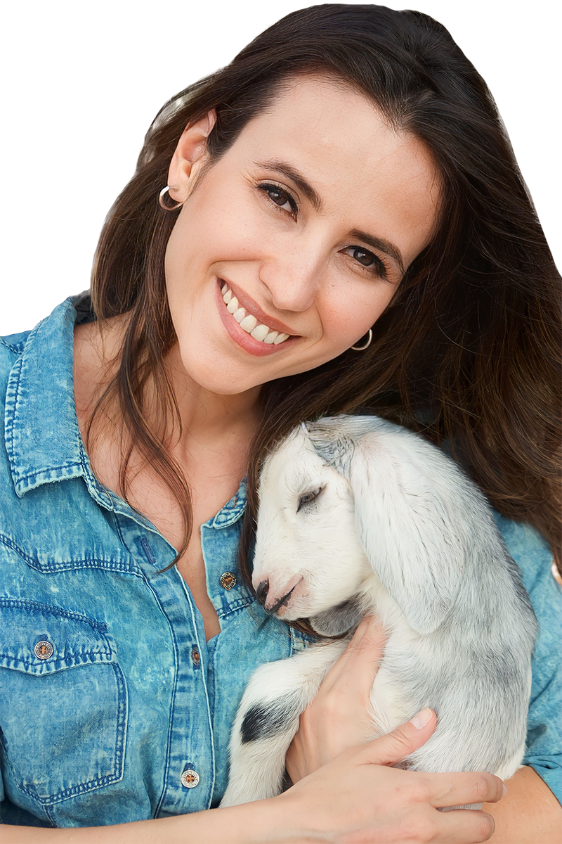 A woman smiling and holding a sleeping baby goat.