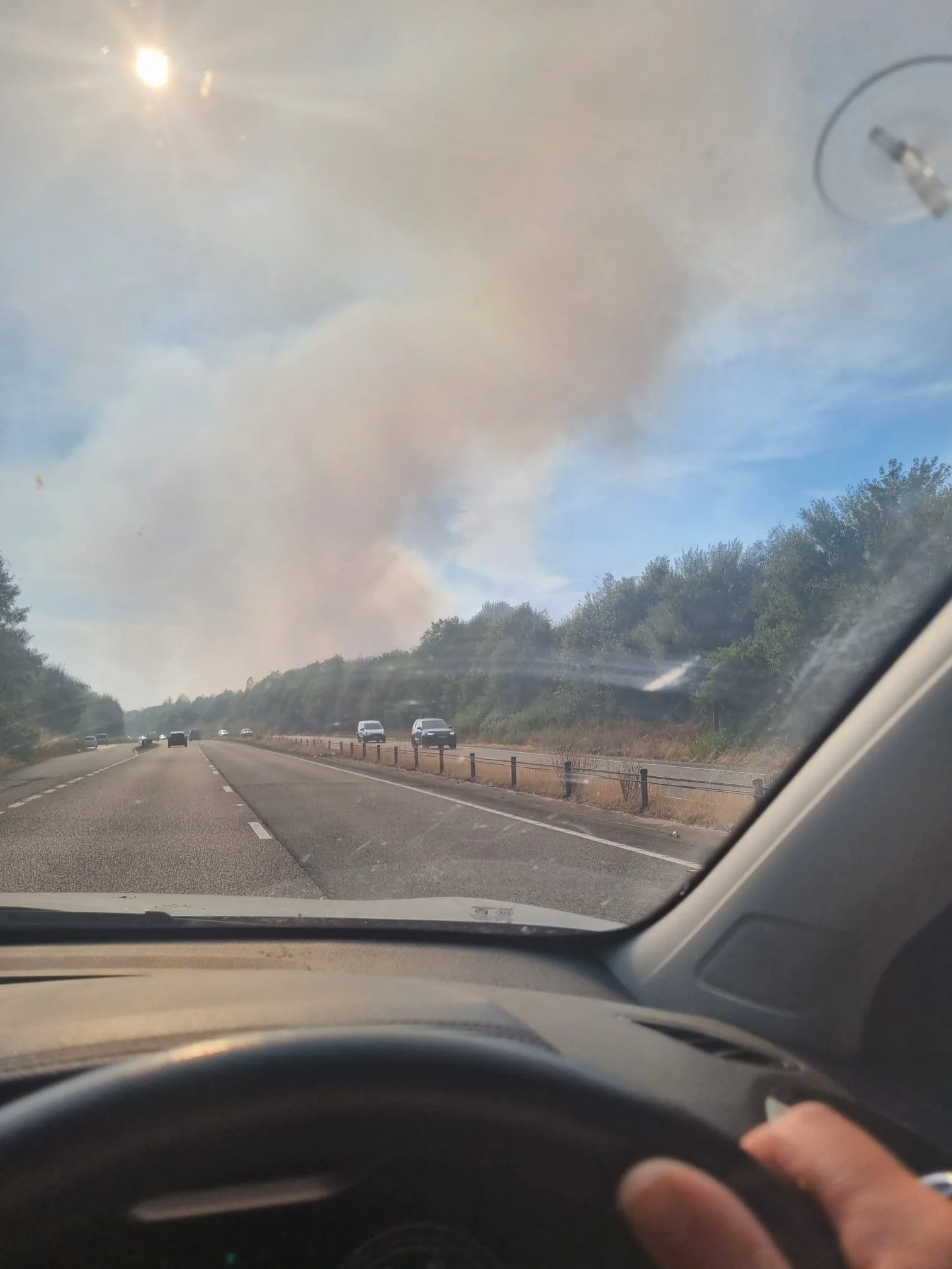 A car driving along a duel carriageway with plumes of smoke ahead from the wildfire