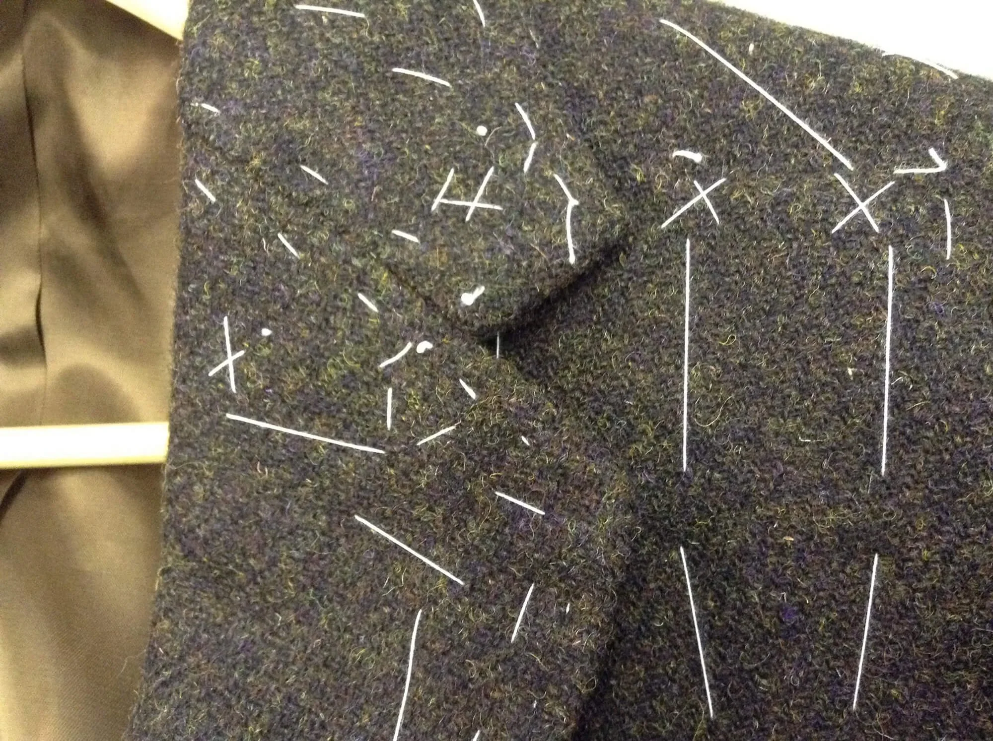 Close-up view of a dark, textured fabric with white lines and symbols stitched onto it, resembling a technical or schematic diagram.