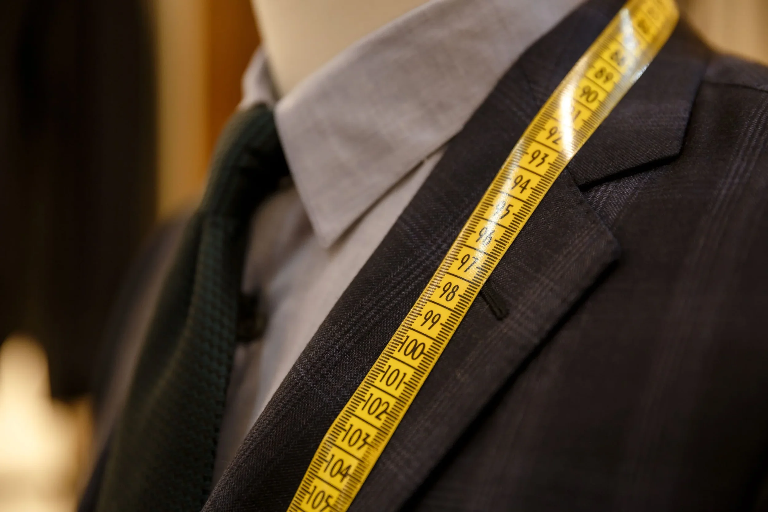 Close-up of a person in a business suit with a yellow measuring tape draped over the shoulder.