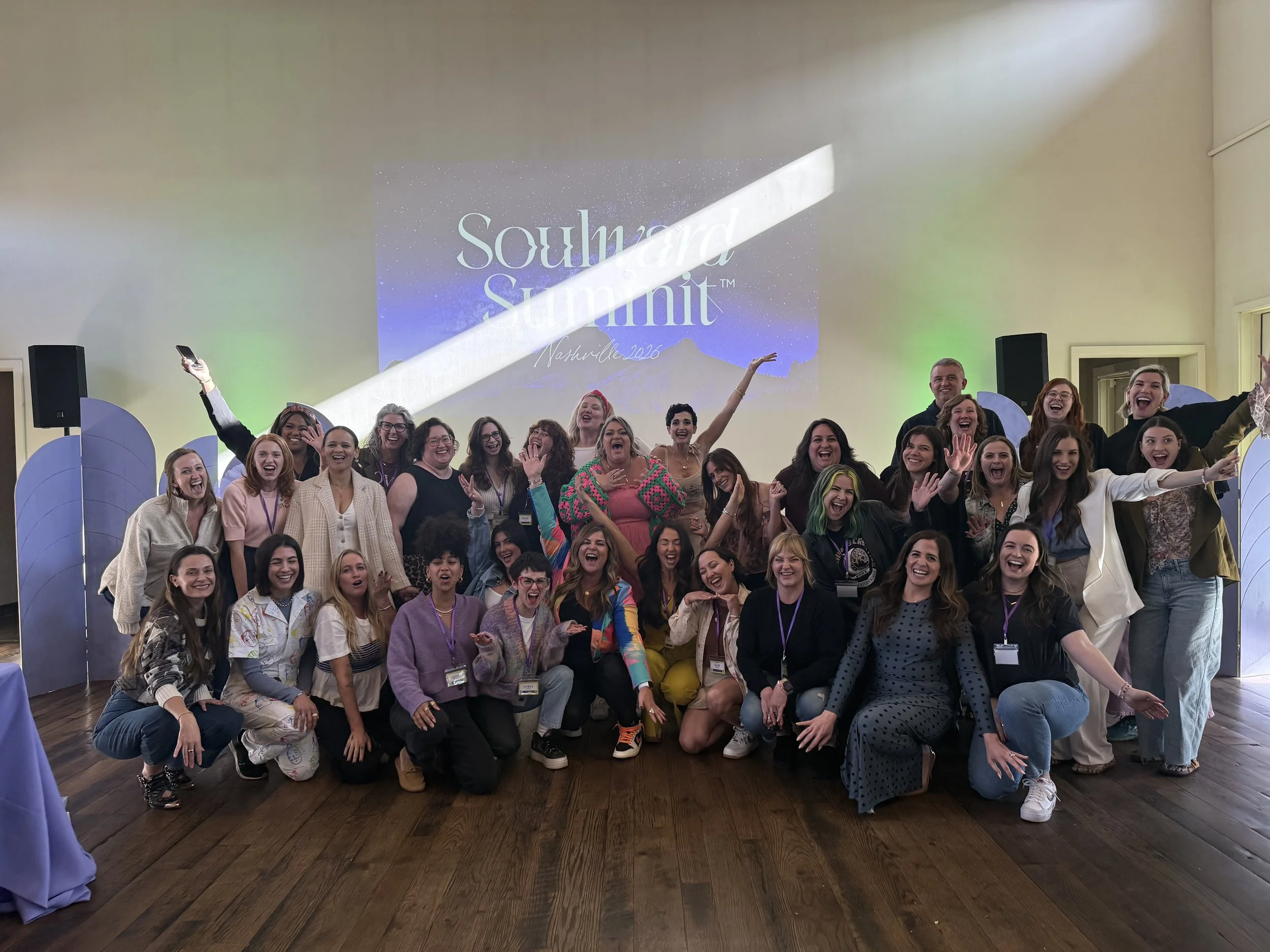 A large group of people, mostly women, posing and smiling for a photo at a conference or event. They are indoors in front of a screen that displays the event name 'Soulward Summit Nashville 2016' and decorative blue panels.