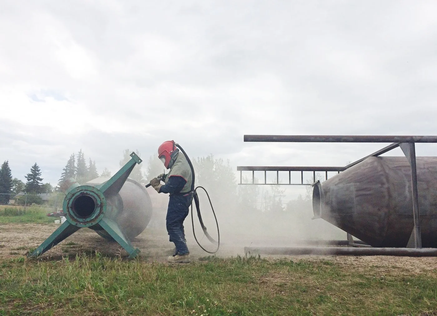 Person sandblasting a metal storage bin