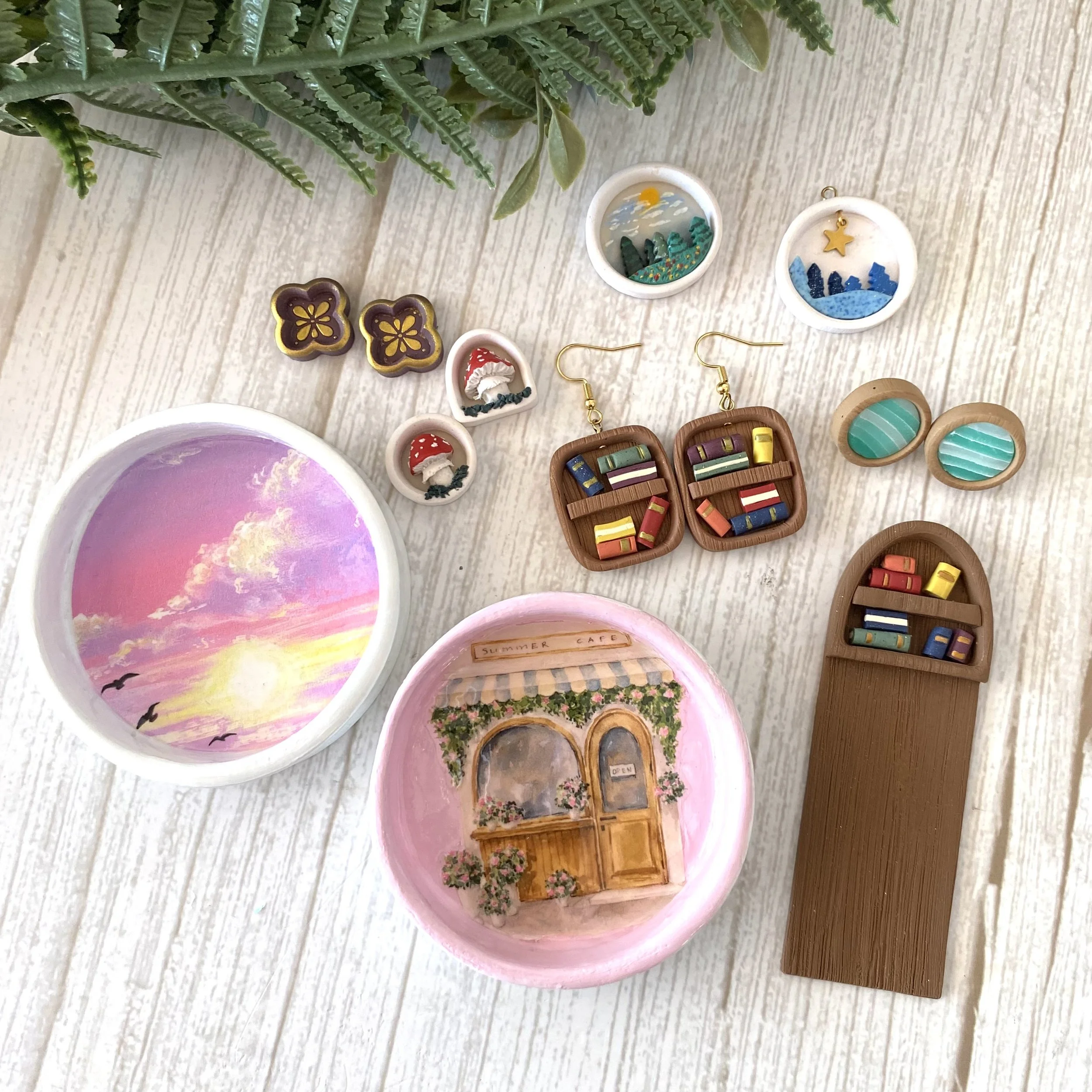 Collection of miniature decorative items including painted bowls, earrings, and tiny furniture models on a light wooden surface.