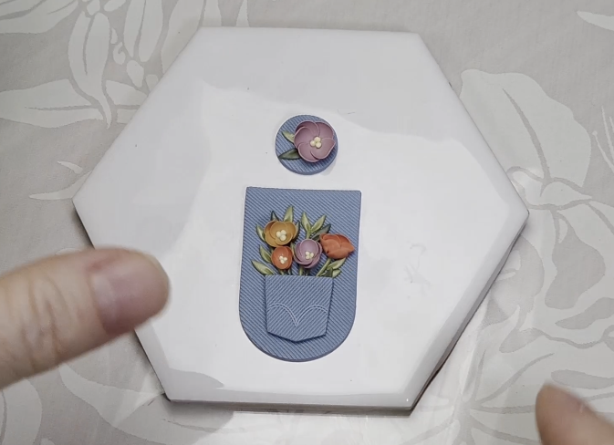 A hexagonal white tray with a paper craft showing a pocket with flowers and an additional flower piece above it.