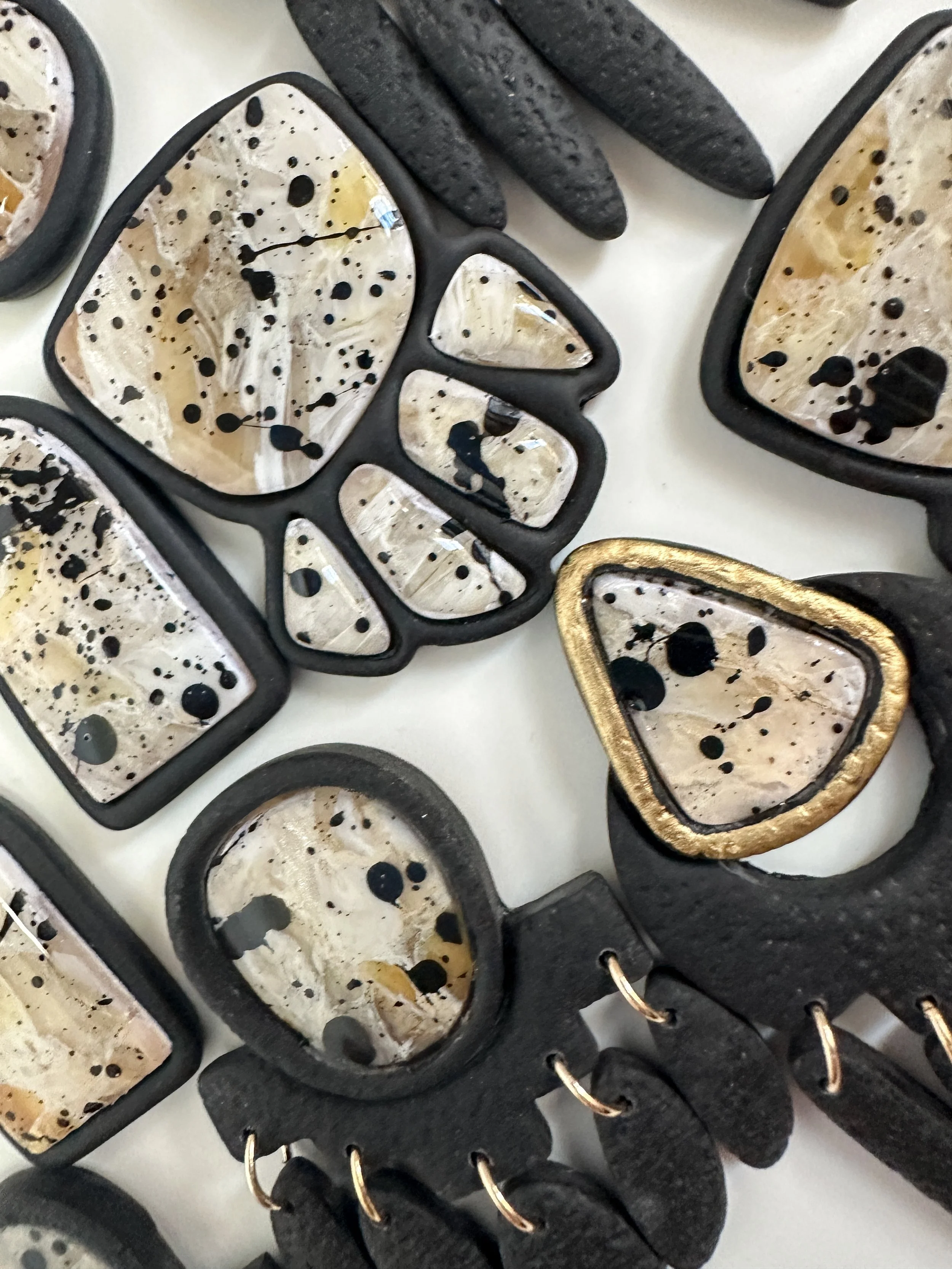Collection of jewelry pieces with cream-colored inlays and black splatter designs, some with black or gold accents.