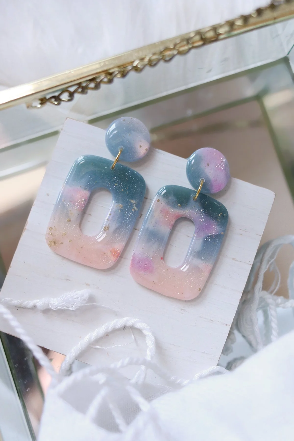 Colorful resin earrings with pastel blue, pink, purple, and gold flecks, hanging on a white card.