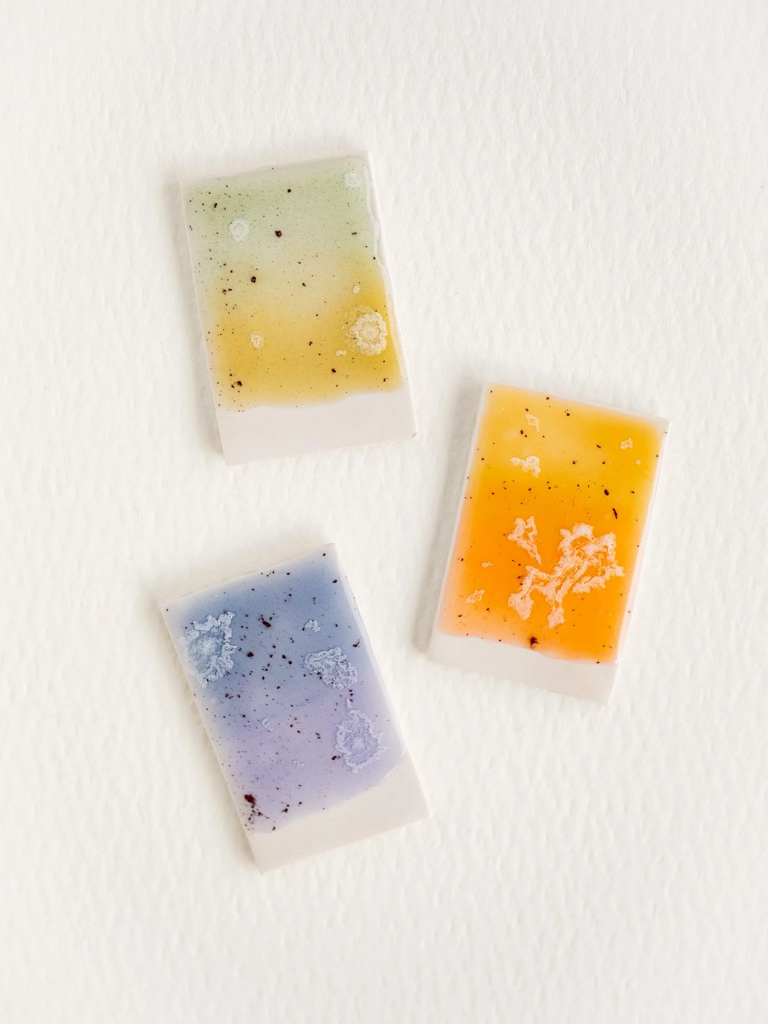 Three small resin soap bars with colored flecks arranged on a white textured background.