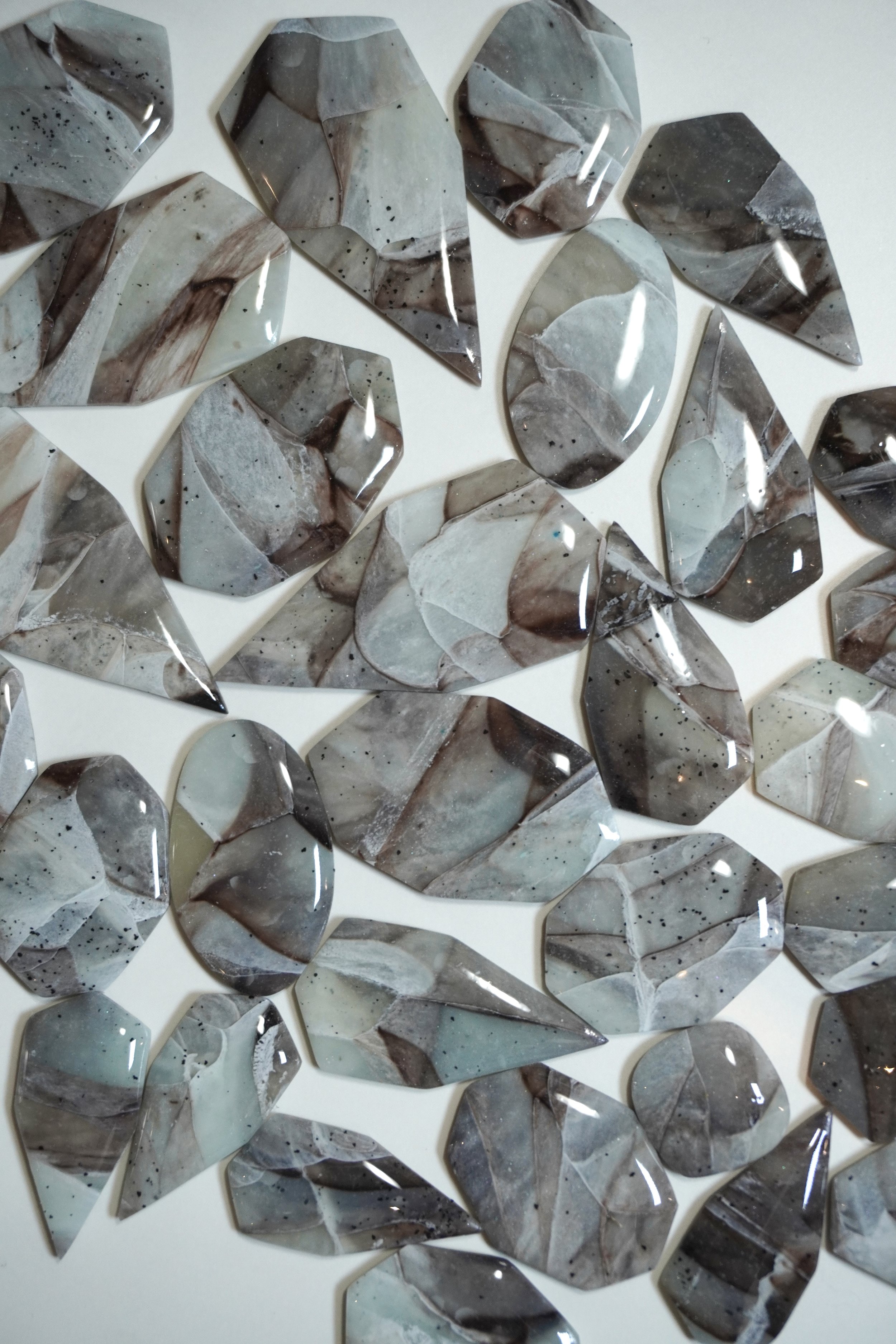 Multiple irregularly shaped pieces of marble with gray, white, and beige colors arranged on a white surface.