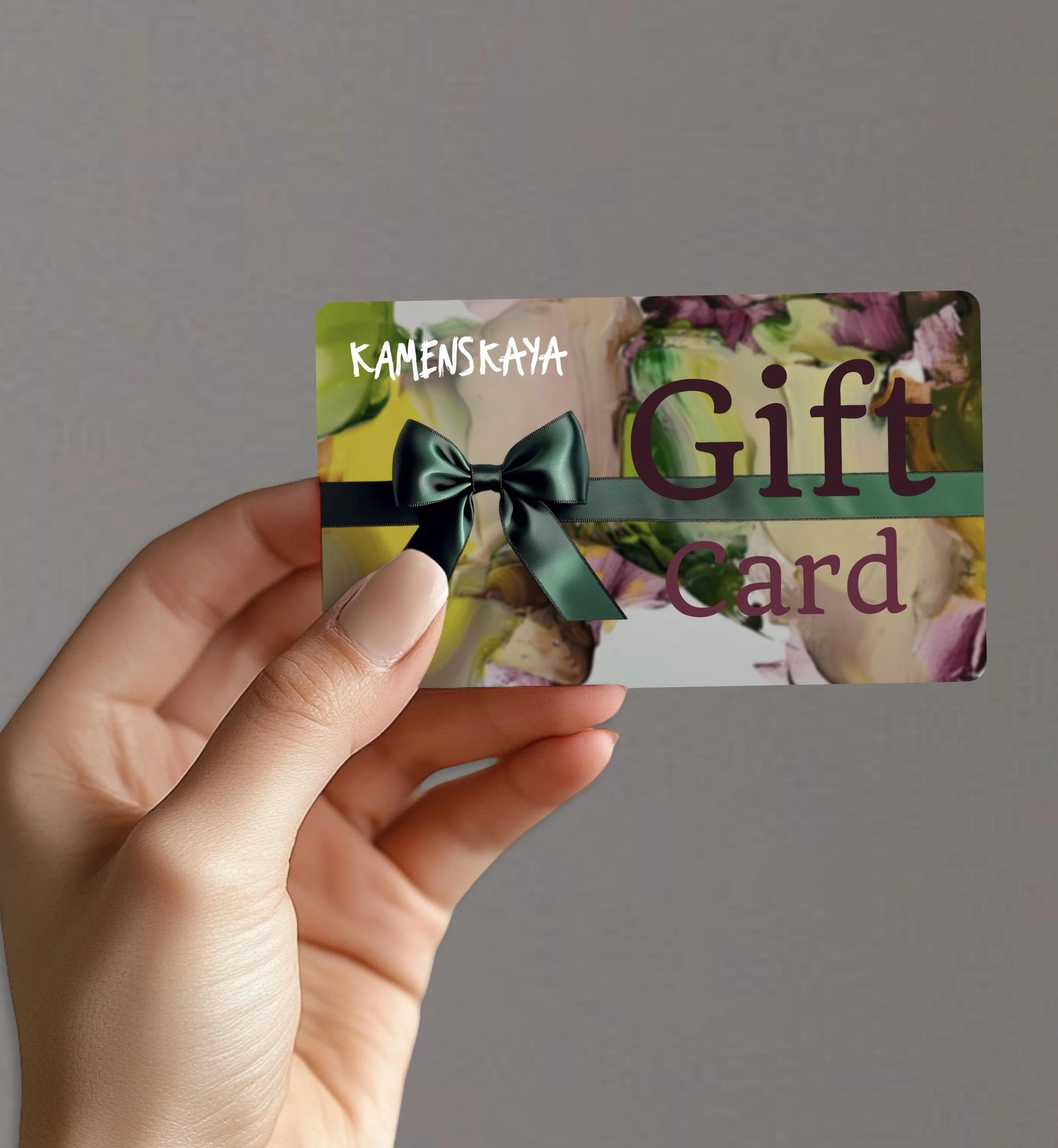 A hand holding a gift card with a floral background, green ribbon, and bow, reading "KAMENSRAYA Gift Card".