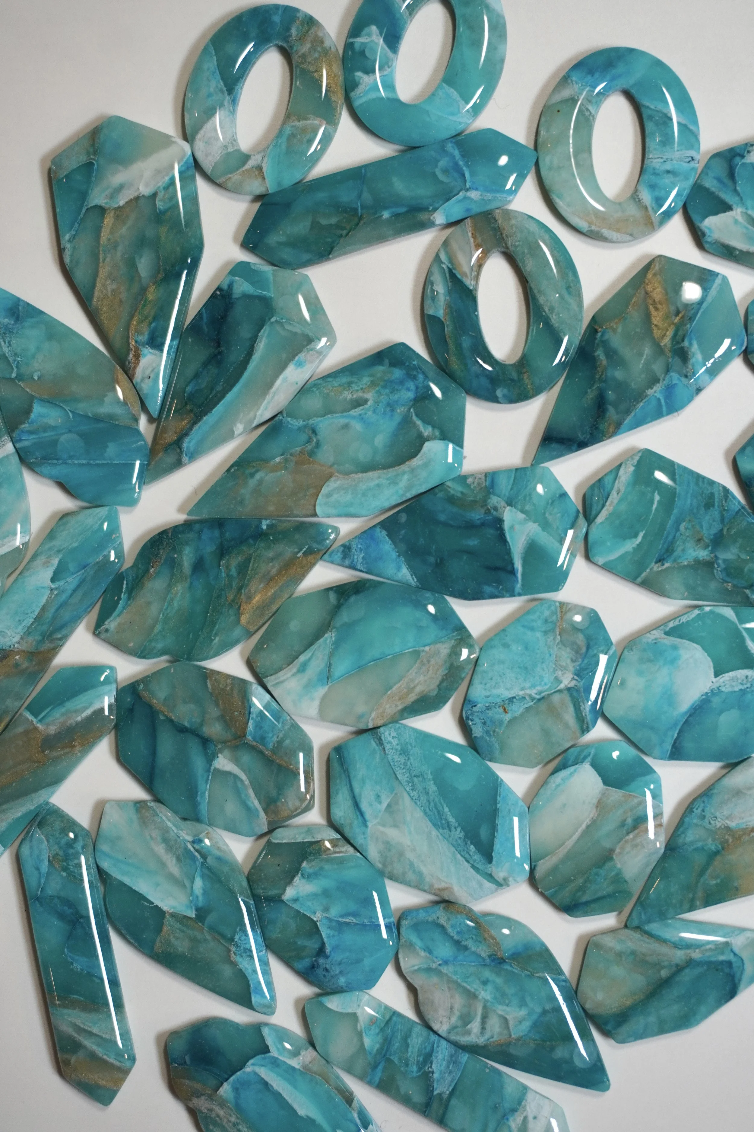 Various blue and green marble-like acrylic or resin pieces shaped like gemstones and rings spread across a white surface.