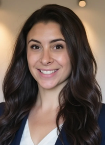 A young woman with long dark hair smiling at the camera, indoors with warm lighting.