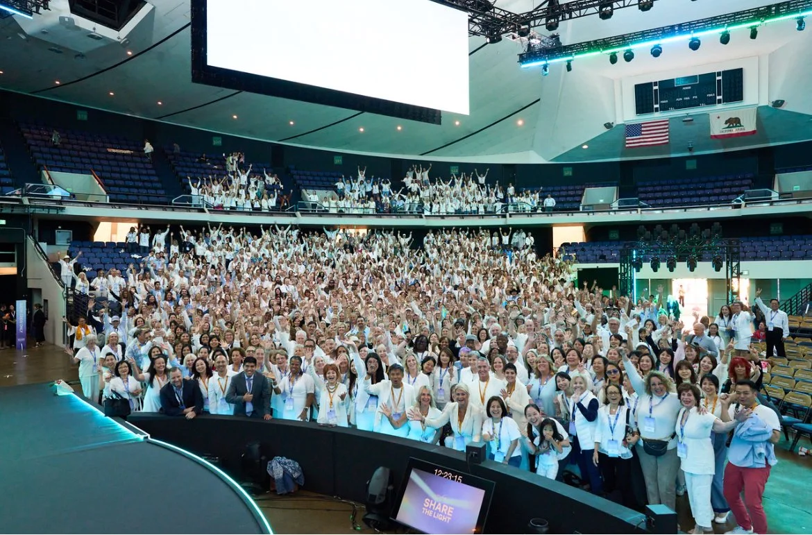 Large group of people in white attire  in audience at an indoor conference or event.