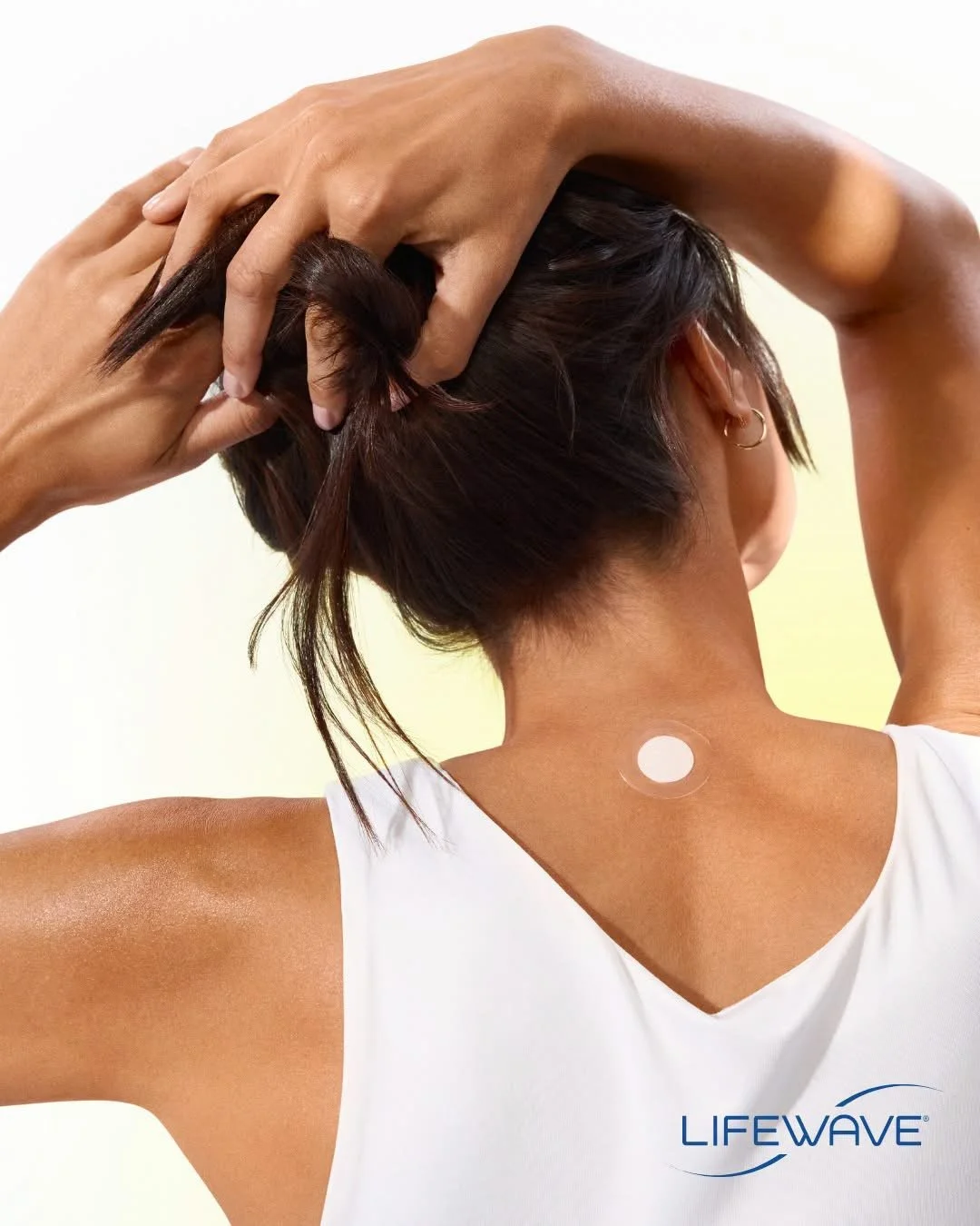 Back view of a woman with a small circular patch on her neck and her hands on her head, demonstrating the use of a Lifewave product.