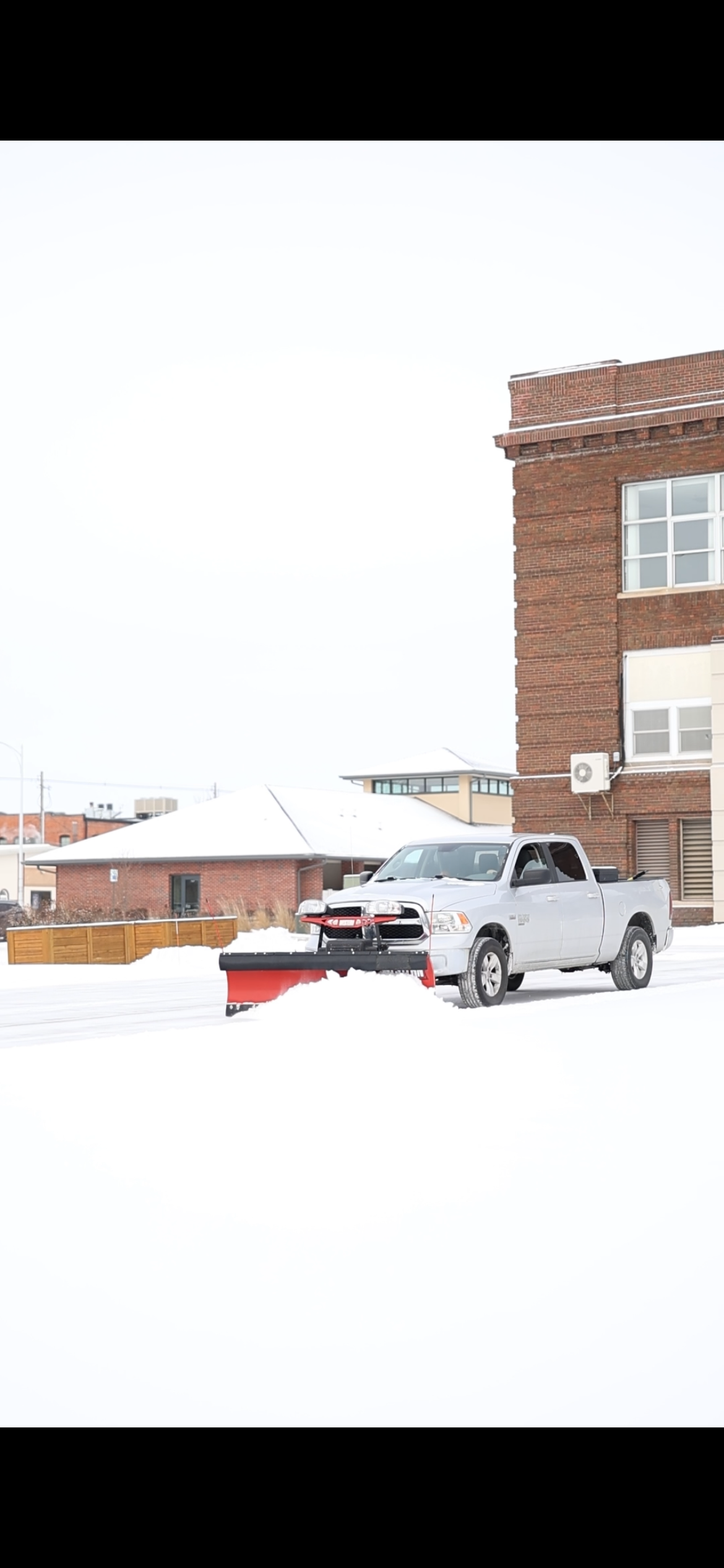 An orange vehicle equipped with a snowplow clearing snow from a road.