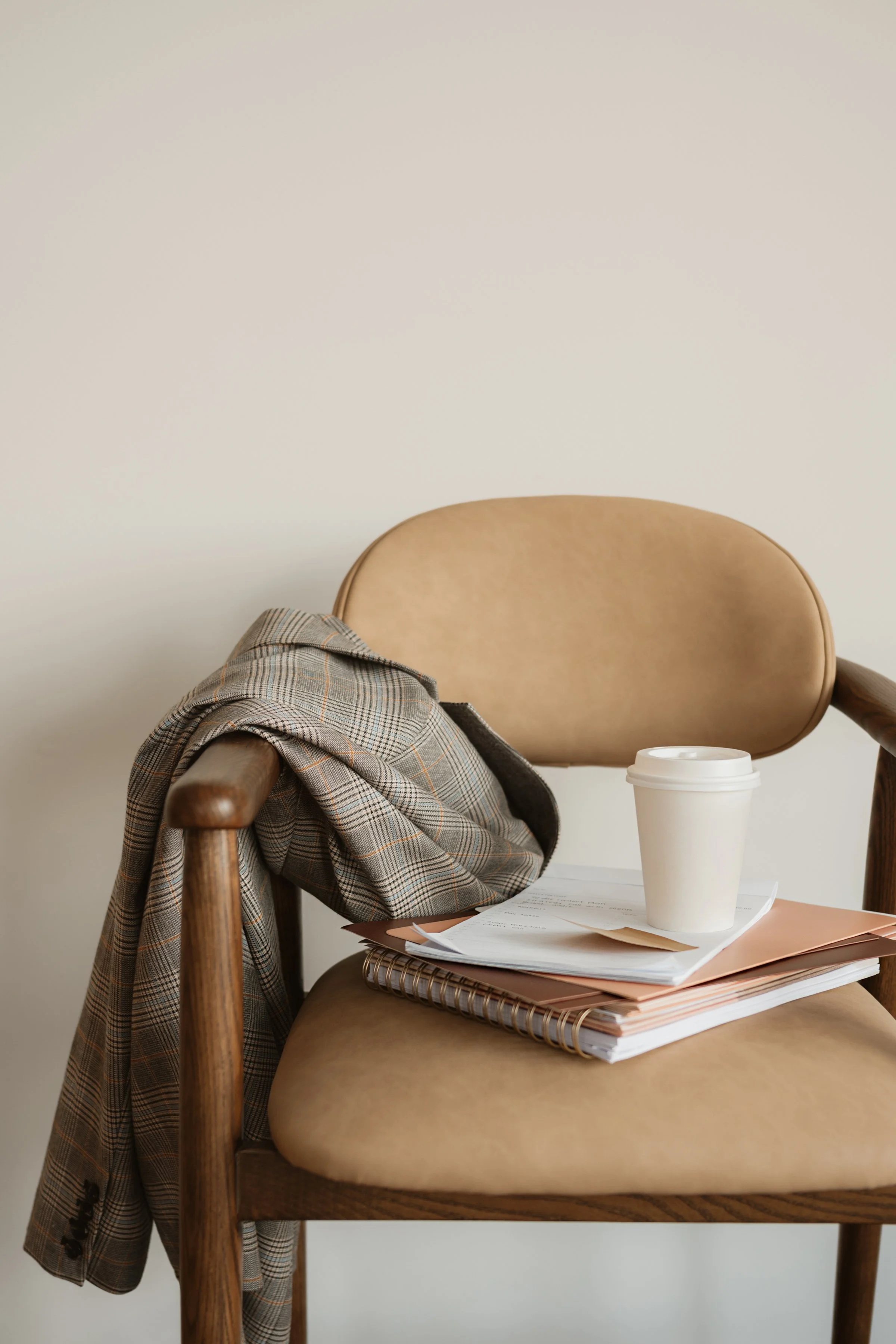 Plaid blazer, notebooks, and coffee cup on a tan leather chair