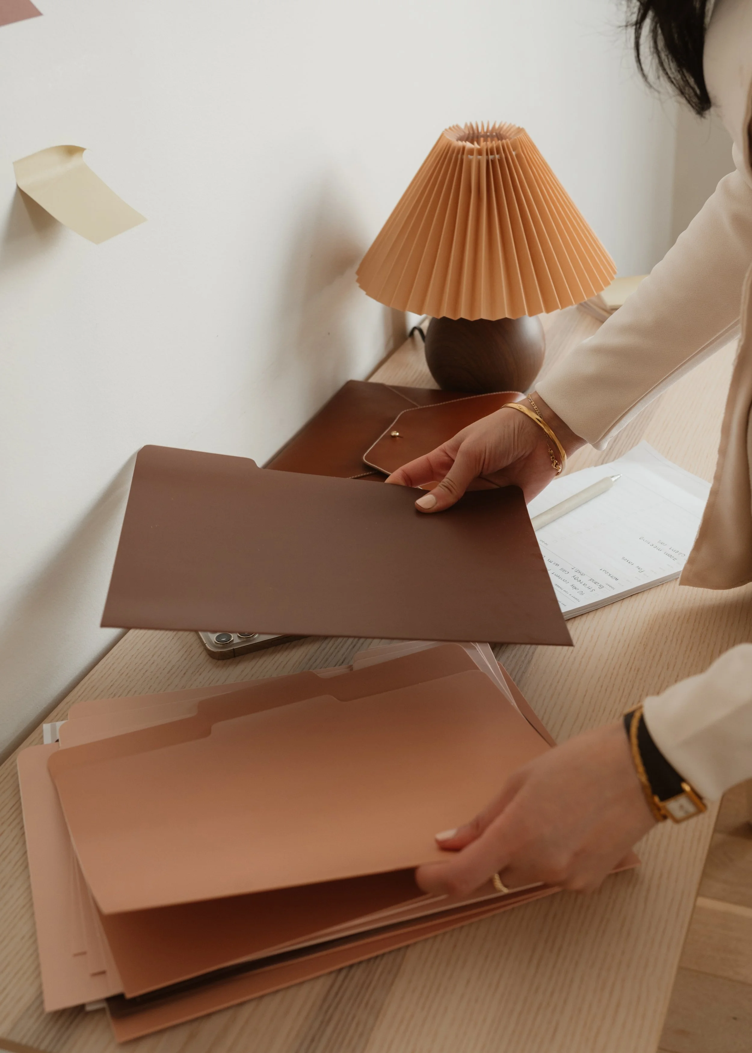 Hands sorting brown file folders on a desk beside a pleated lamp