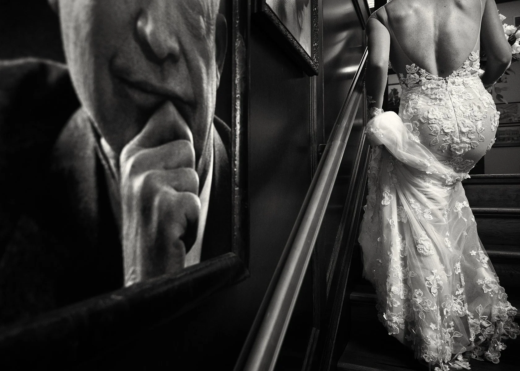 A portrait of a man with a finger to his lips, and a wedding dress displayed on a staircase near the wall.